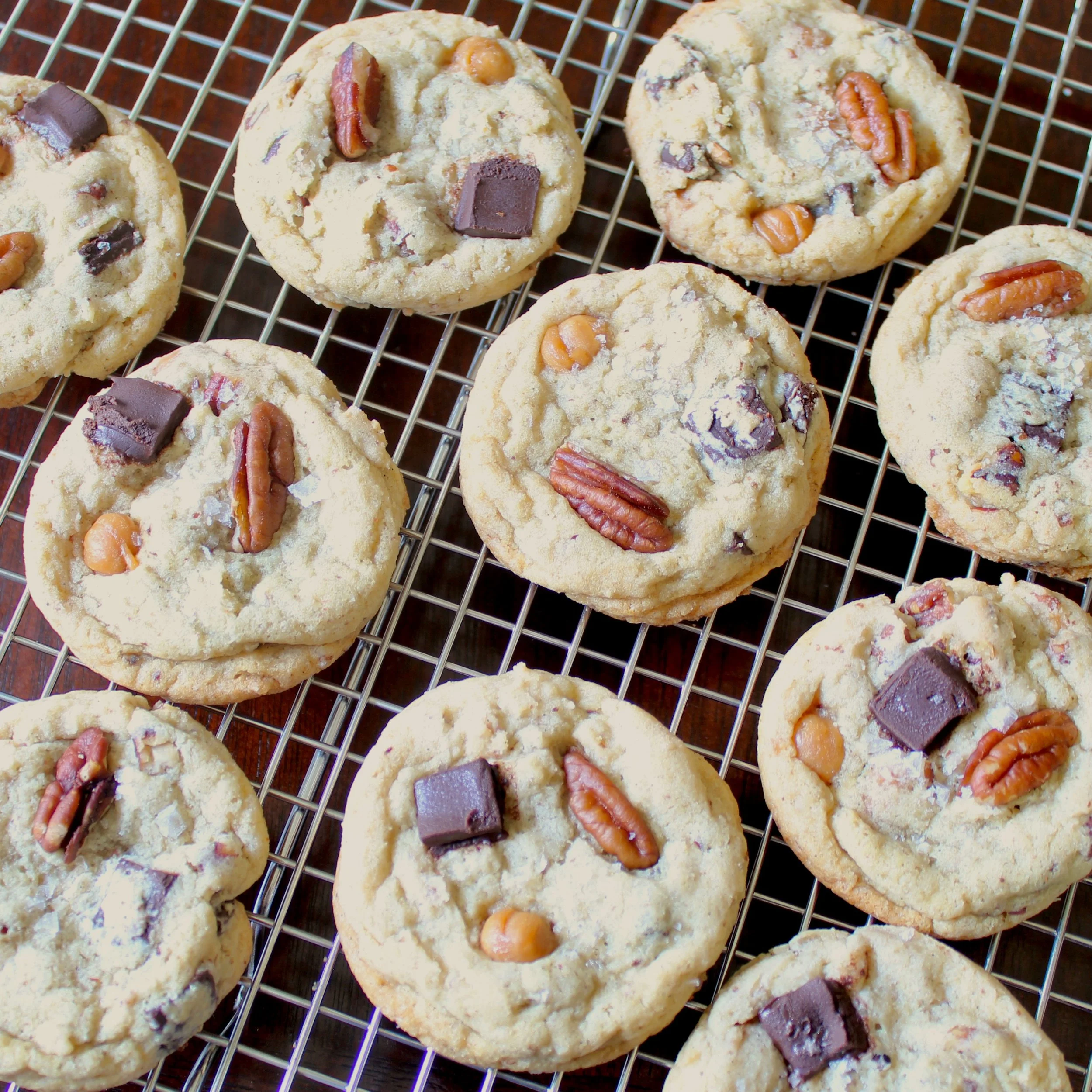 Freshly baked cookies topped with whole pecans and chocolate chunks cooling on a wire rack.