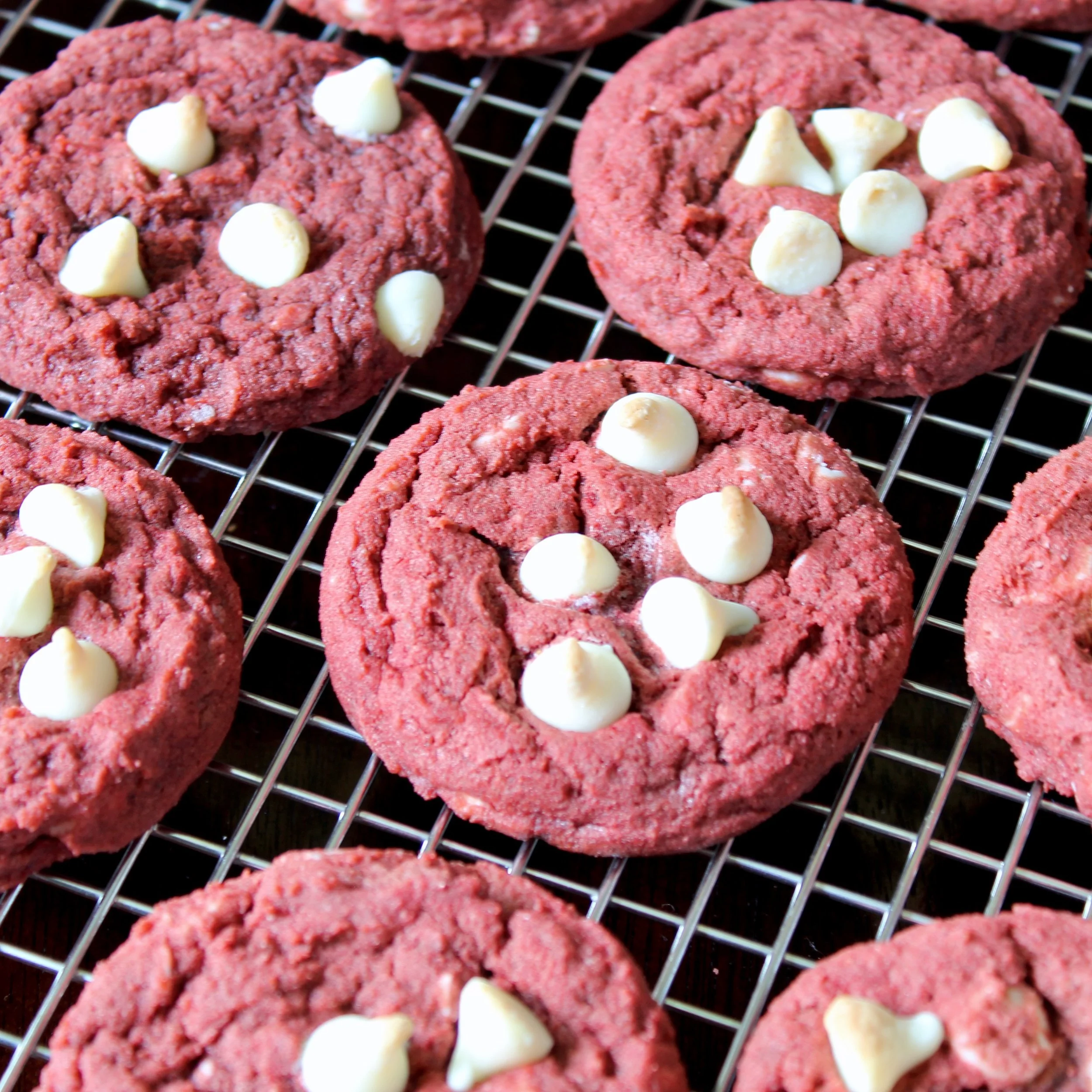 Close-up angle of soft red velvet cookies loaded with white chocolate chips cooling on a metal wire rack.