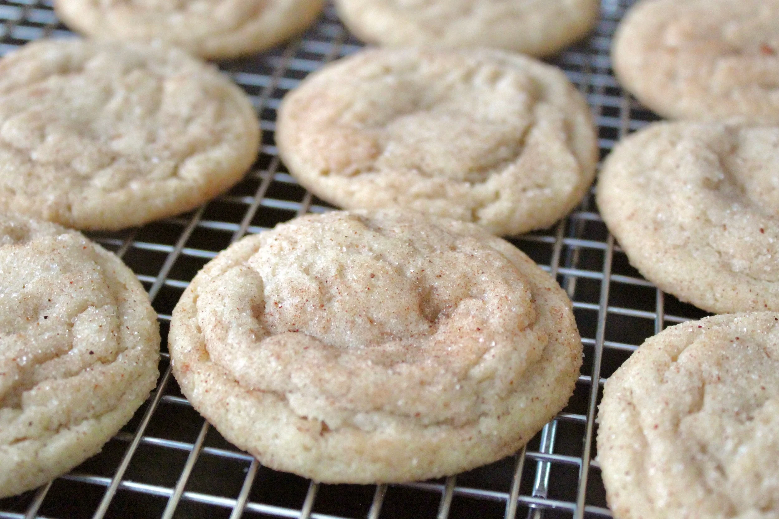 Freshly baked snickerdoodle cookies cooling on a wire rack, showing a crinkled texture and cinnamon sugar dust.