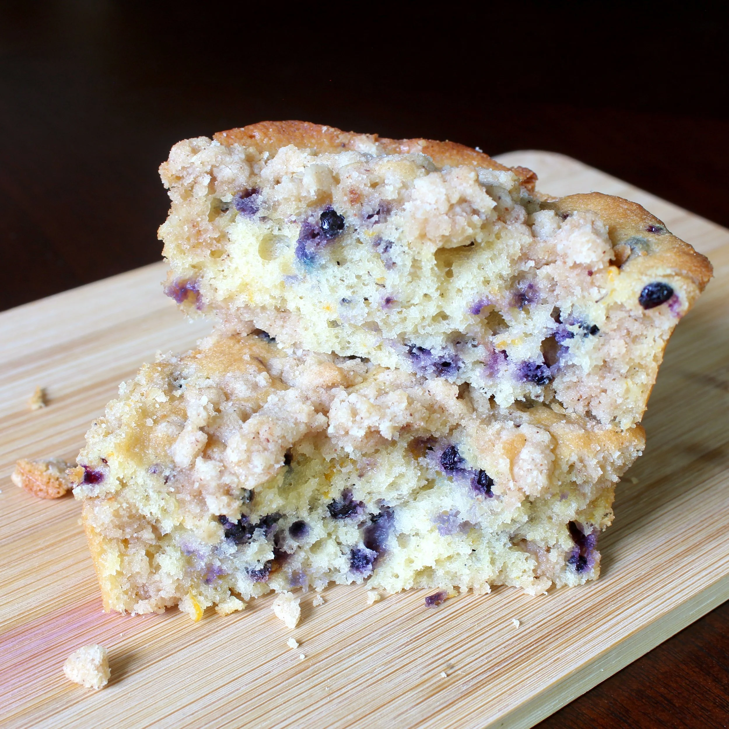 Two stacked halves of a elderberry coffee cake on a light bamboo board, showing the studded berry crumb and streusel top.