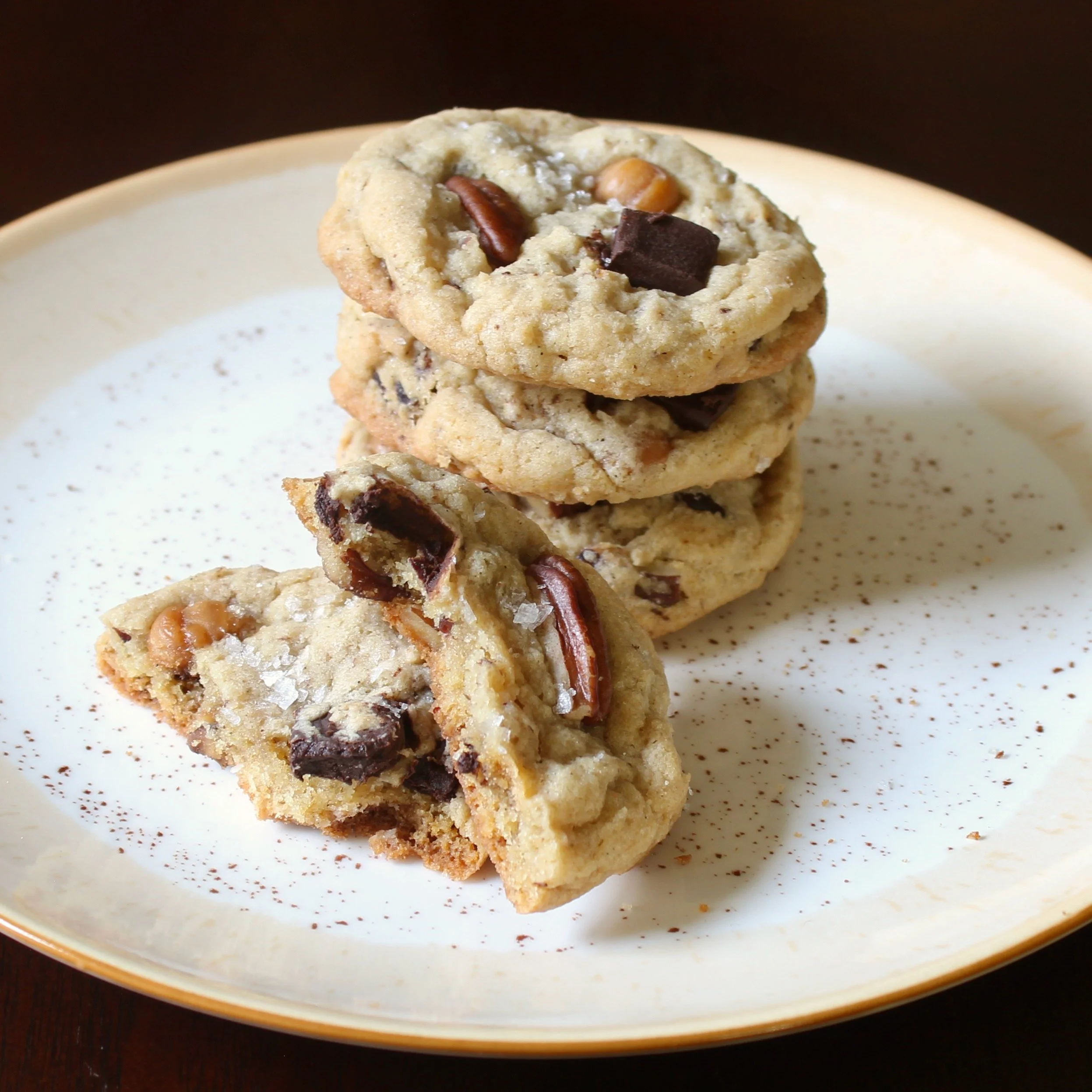 A stack of decadent turtle cookies on a cream plate, with one broken cookie showing the soft inside.