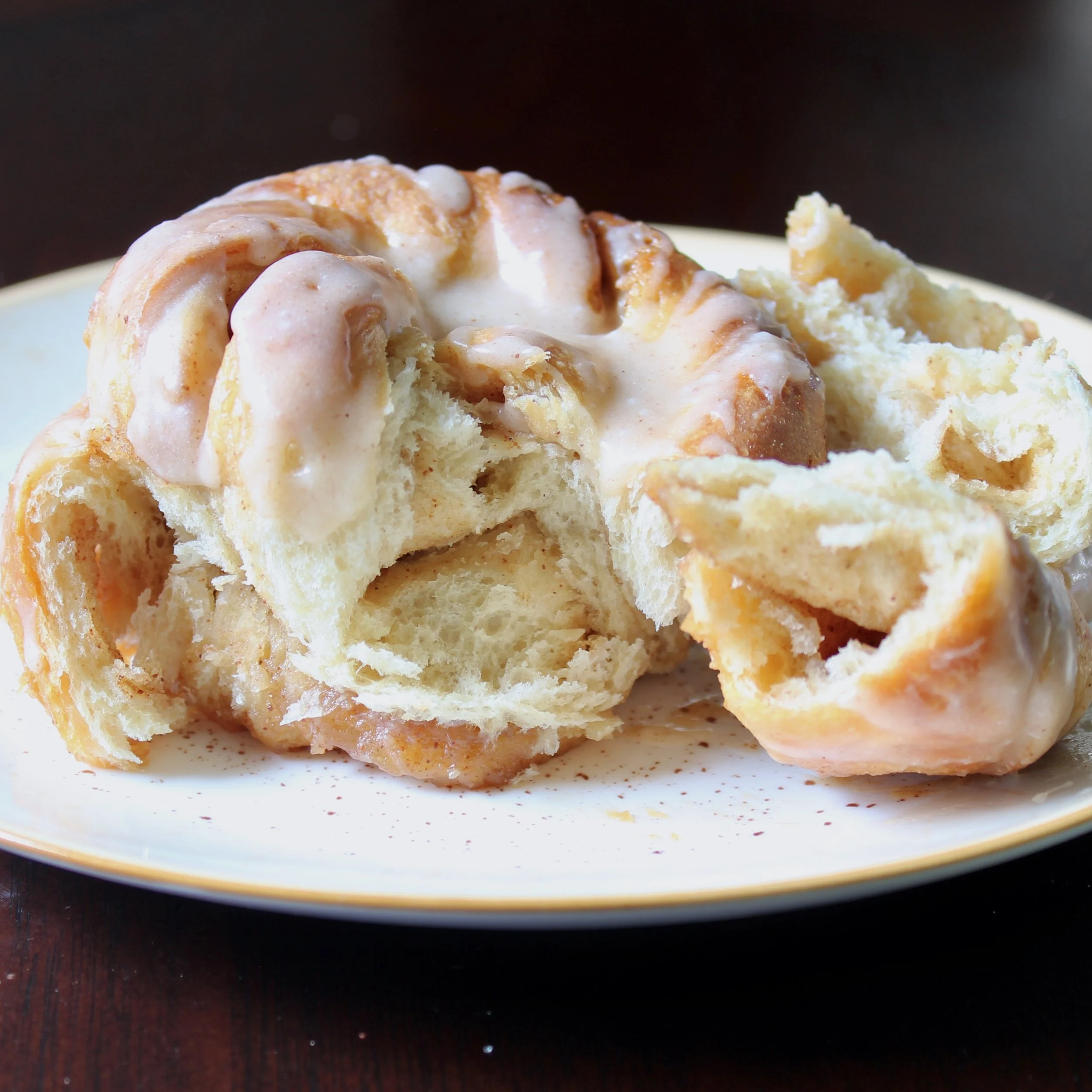 Soft cinnamon babka bun pulled open on a white plate, showing the fluffy layers and sweet glaze drizzled on top.