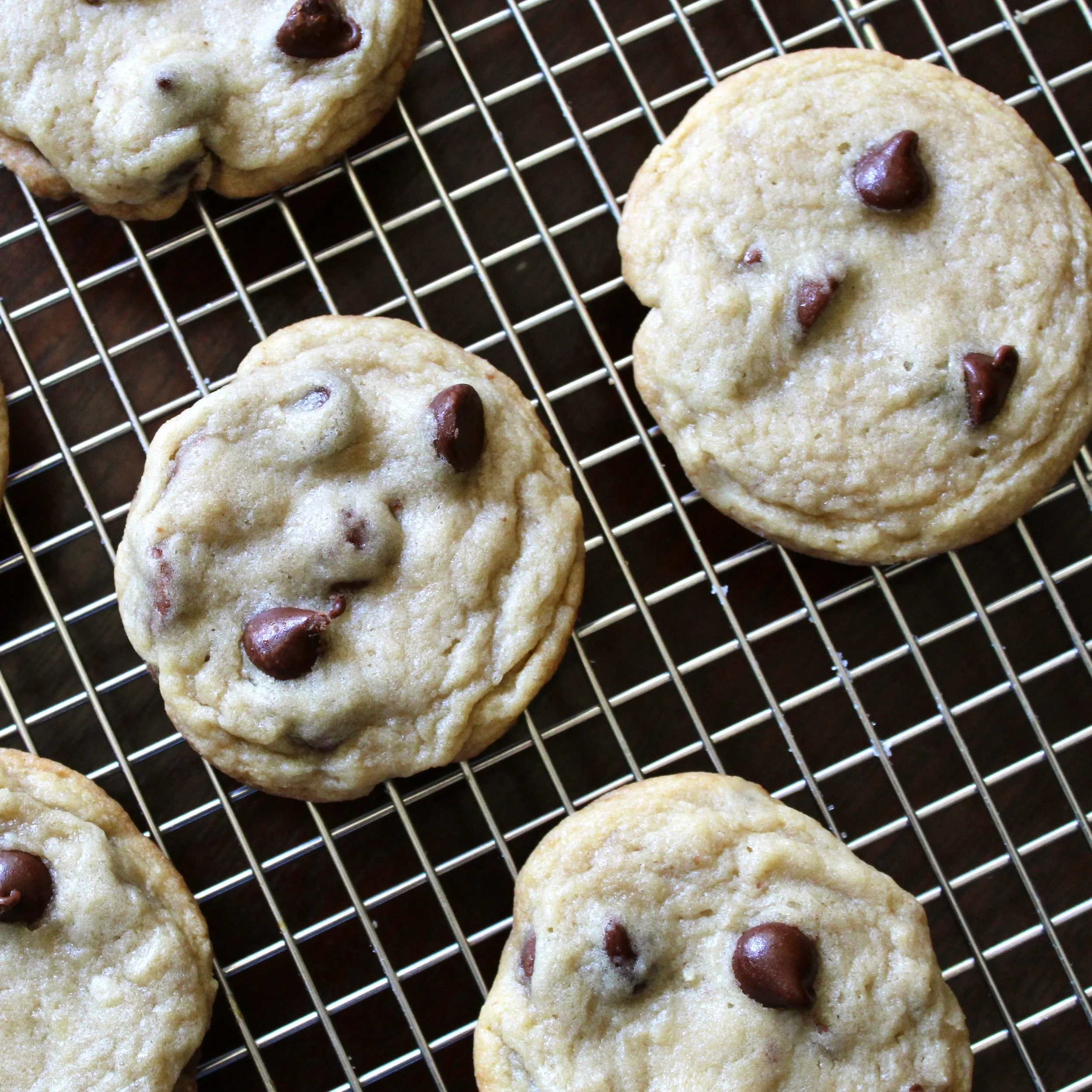 Top-down view of several round, golden-brown chocolate chip cookies cooling on a wire baking rack.