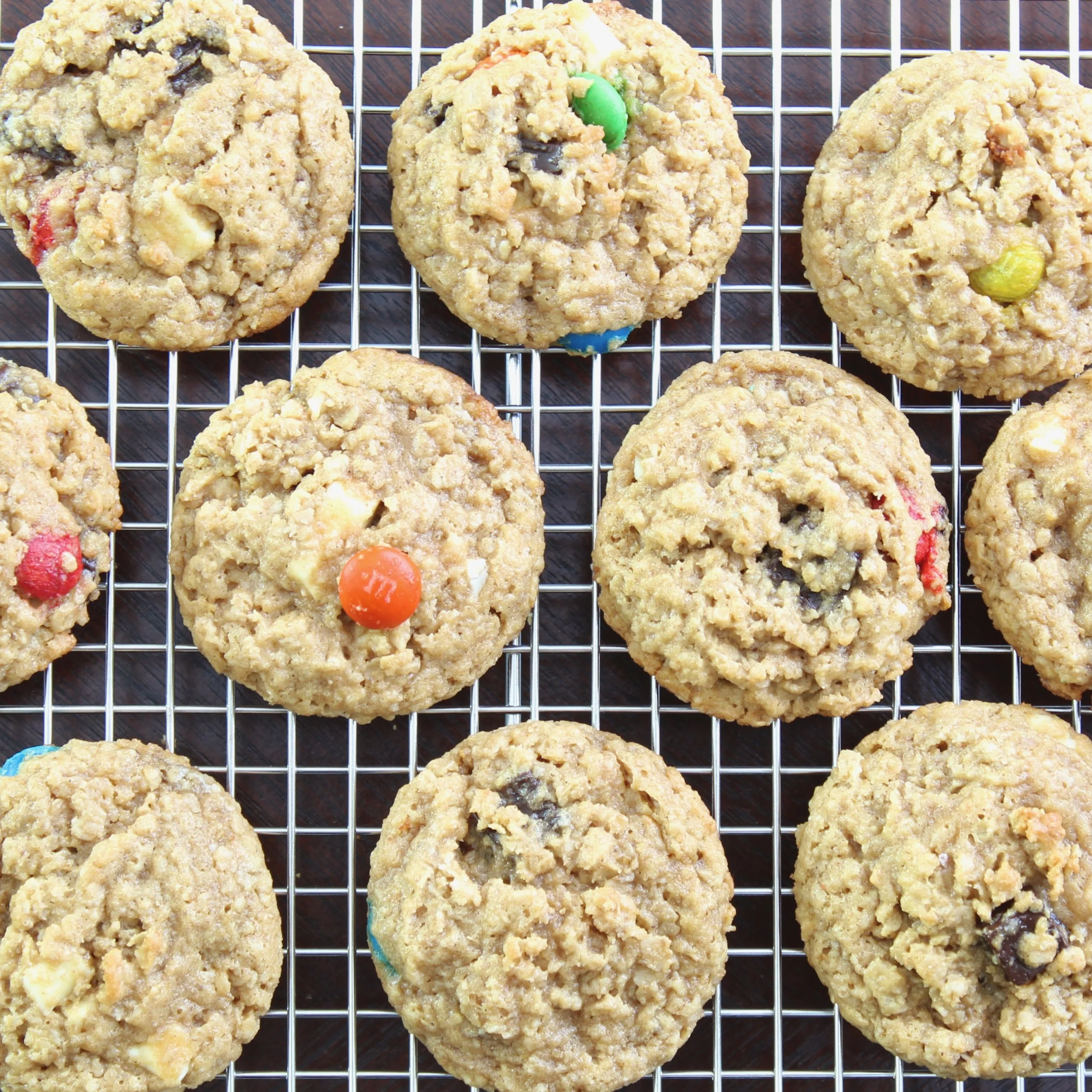 Overhead view of oatmeal monster cookies with candy coated chocolates resting on a wire cooling rack.