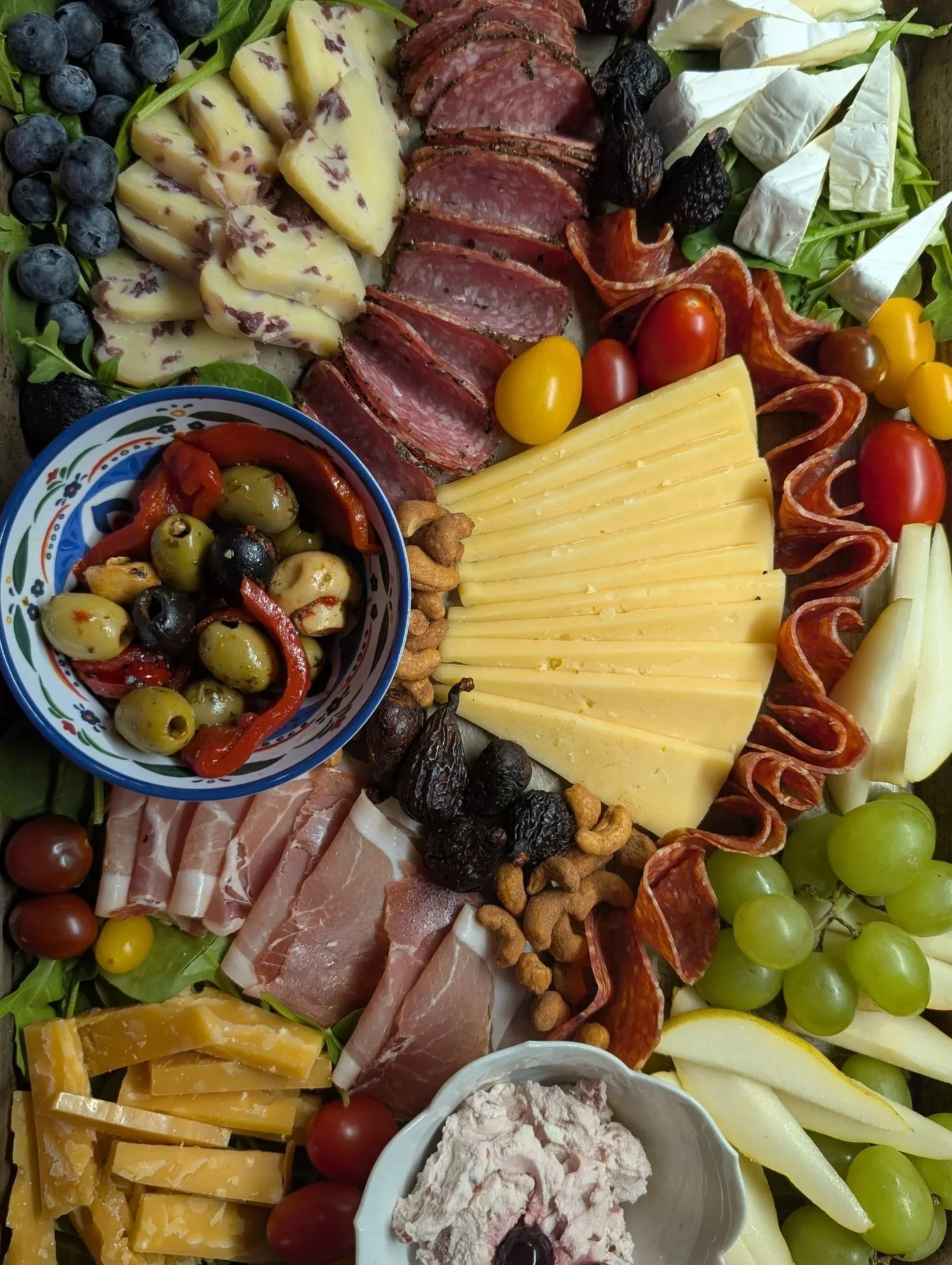 Assorted cheese, meats, fruits, nuts, and olives on a charcuterie board.