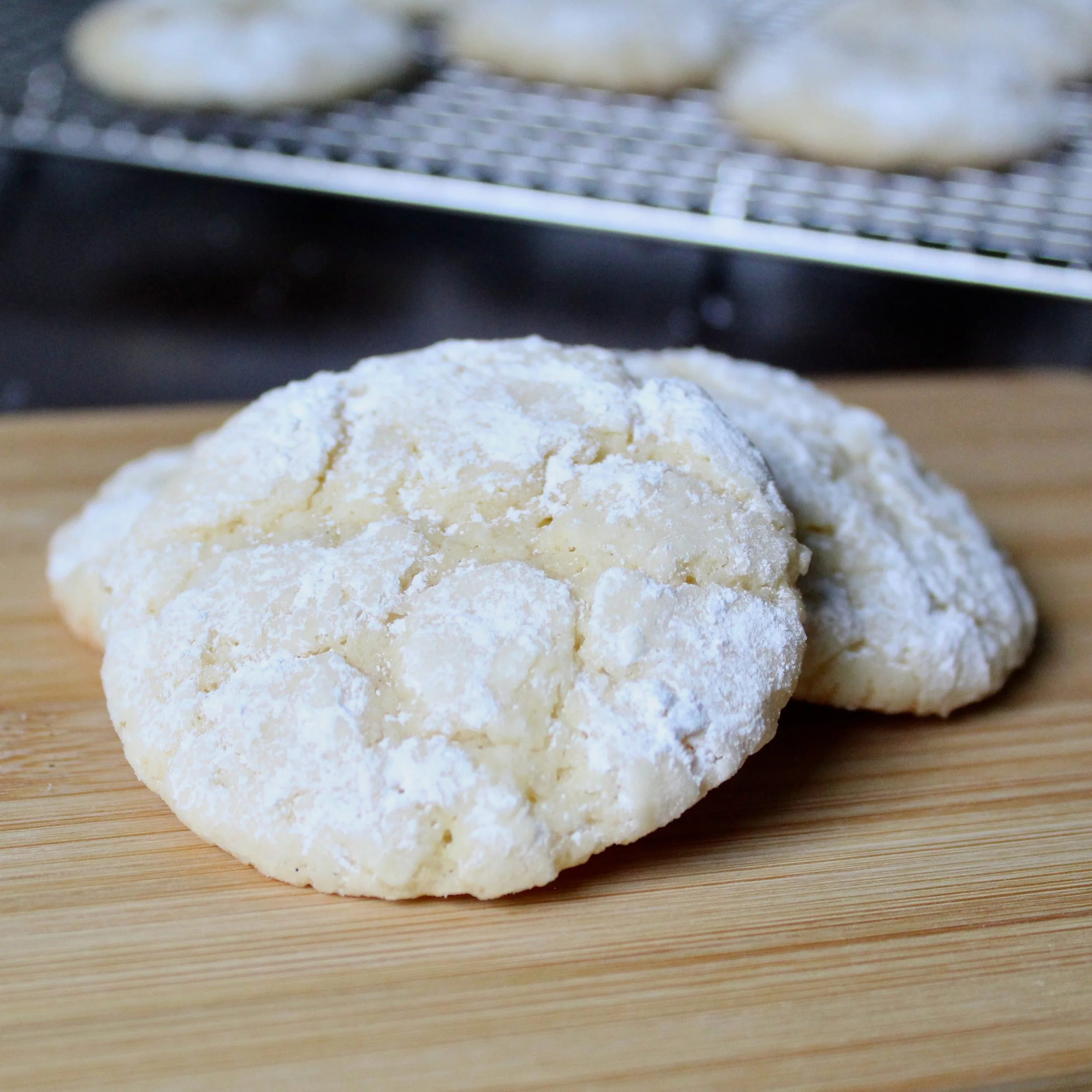 Three soft lemon crinkle cookies coated in powdered sugar rest on a light wooden surface.