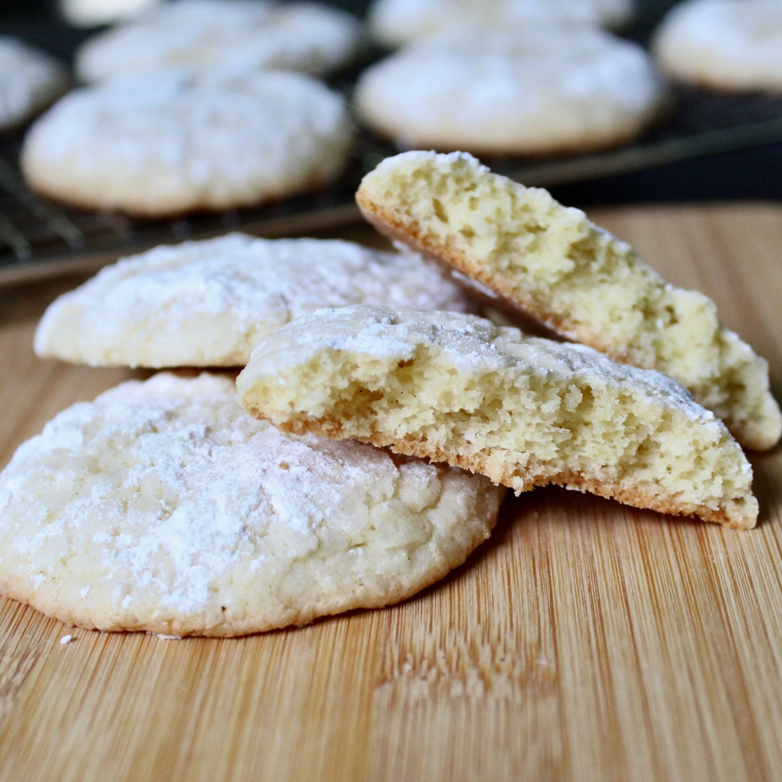 A lemon crinkle cookie broken in half reveals a soft interior, stacked on a wooden board.