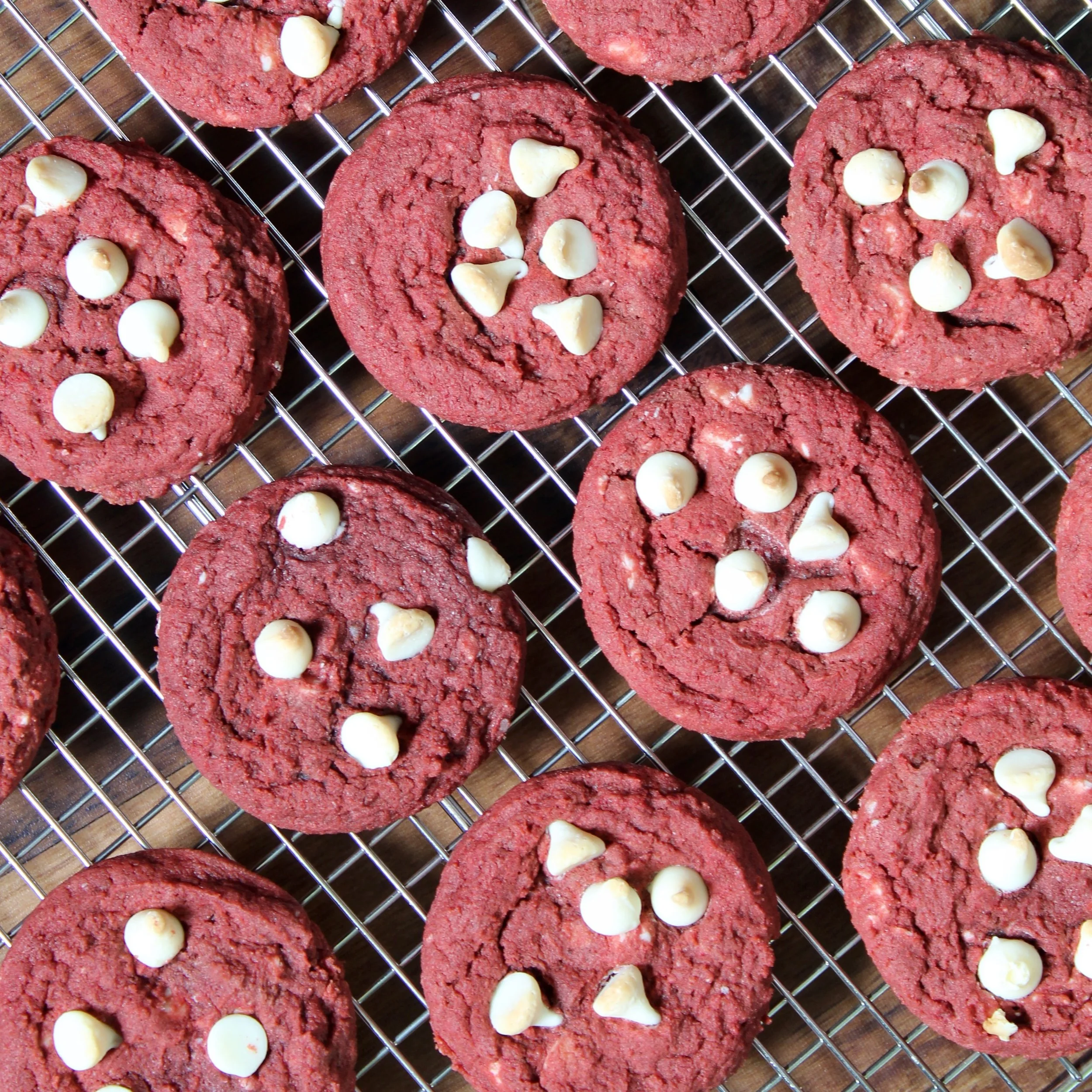 Overhead view of fresh red velvet white chocolate chip cookies cooling on a wire rack.