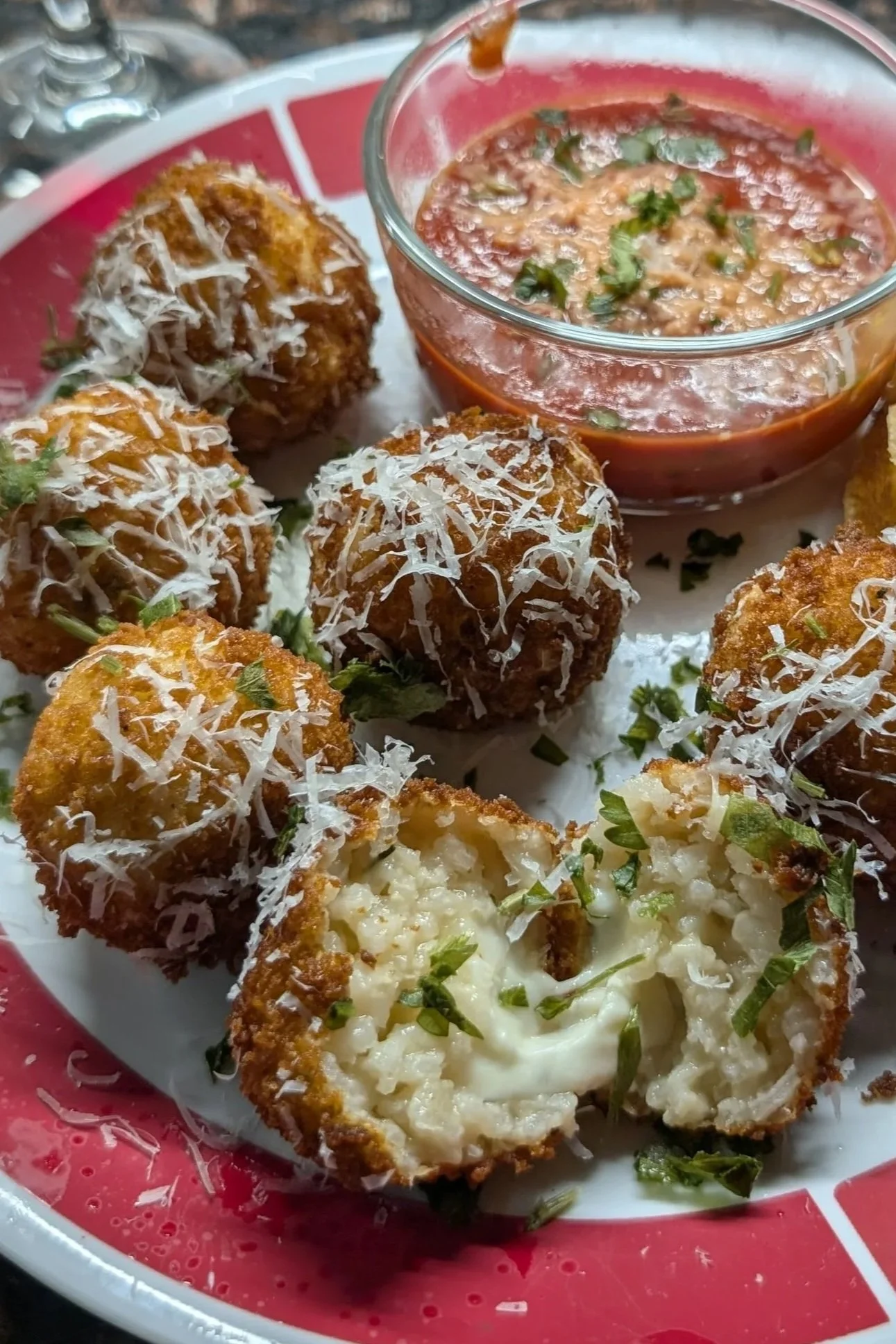 Arancini with grated parmiggiano reggiano and fresh herbs served with a small bowl of tomato dipping sauce.