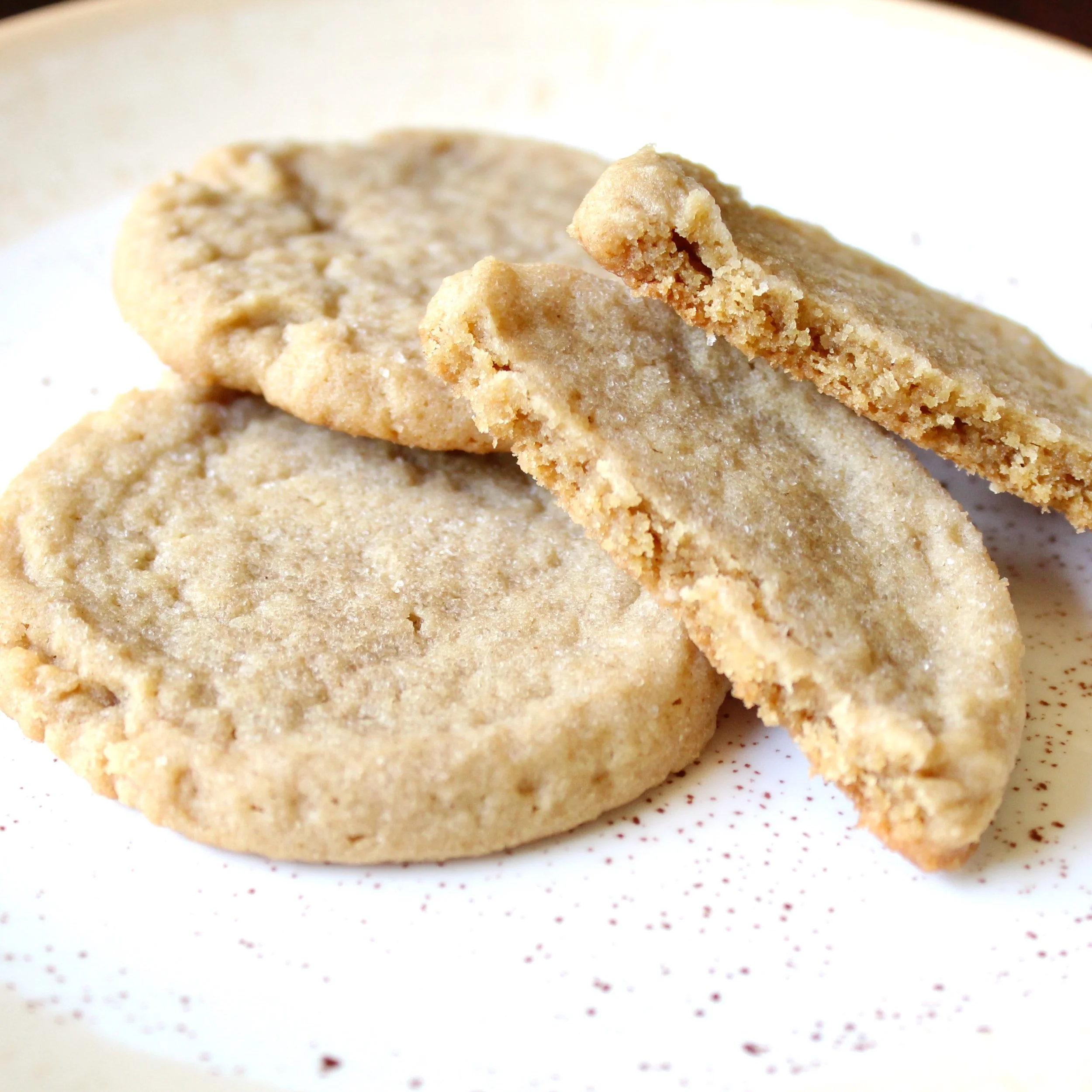 Three peanut butter cookies on a plate, with one broken open to show a soft, chewy texture.