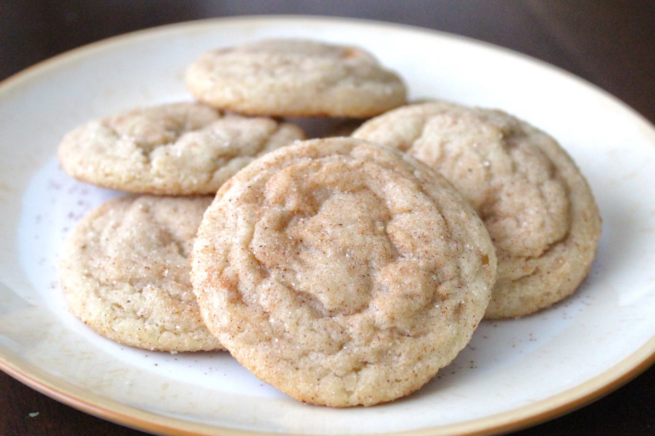 A small stack of soft snickerdoodle cookies coated in cinnamon sugar, served on a rimmed white plate.