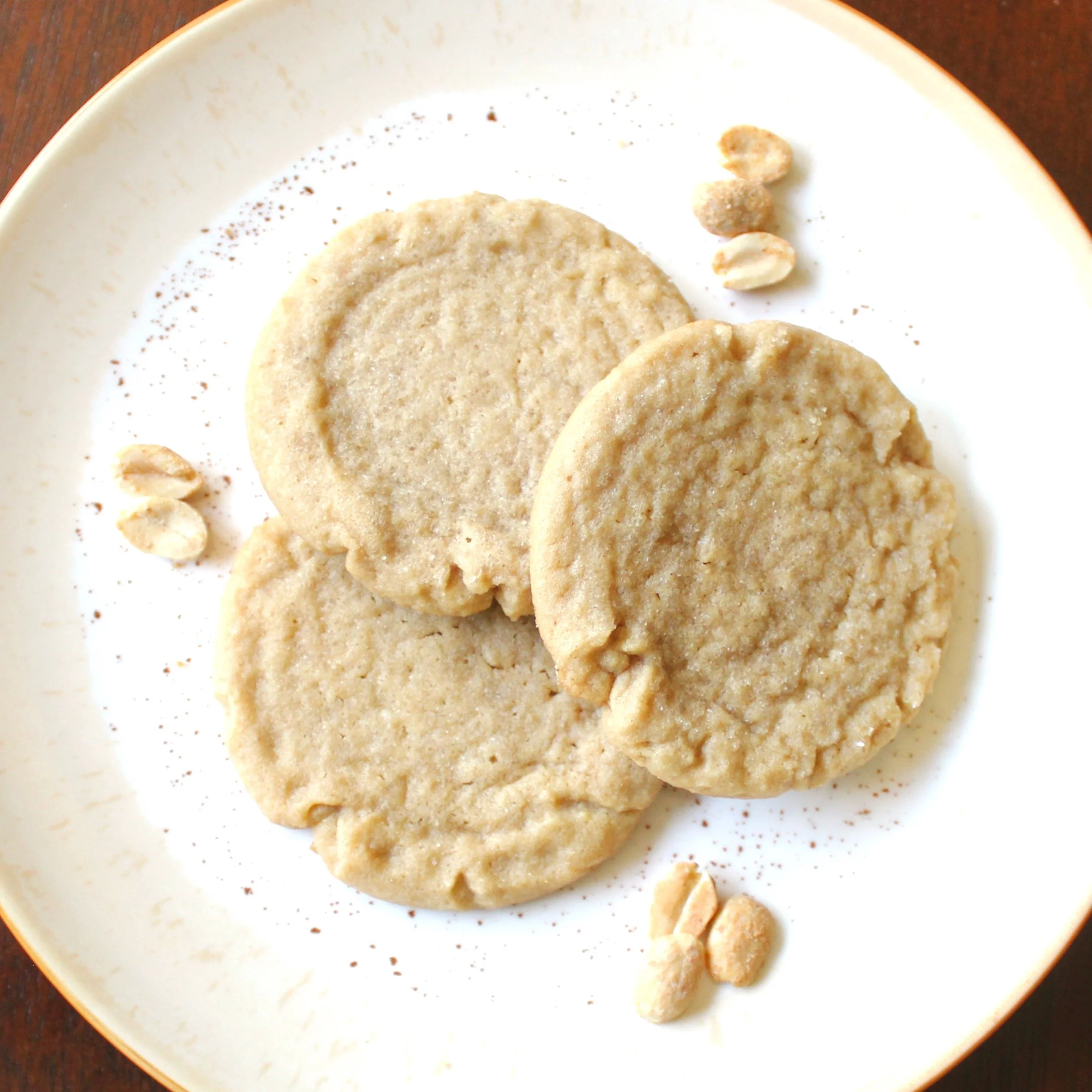 Overhead view of three peanut butter cookies on a white plate accented with loose peanuts.