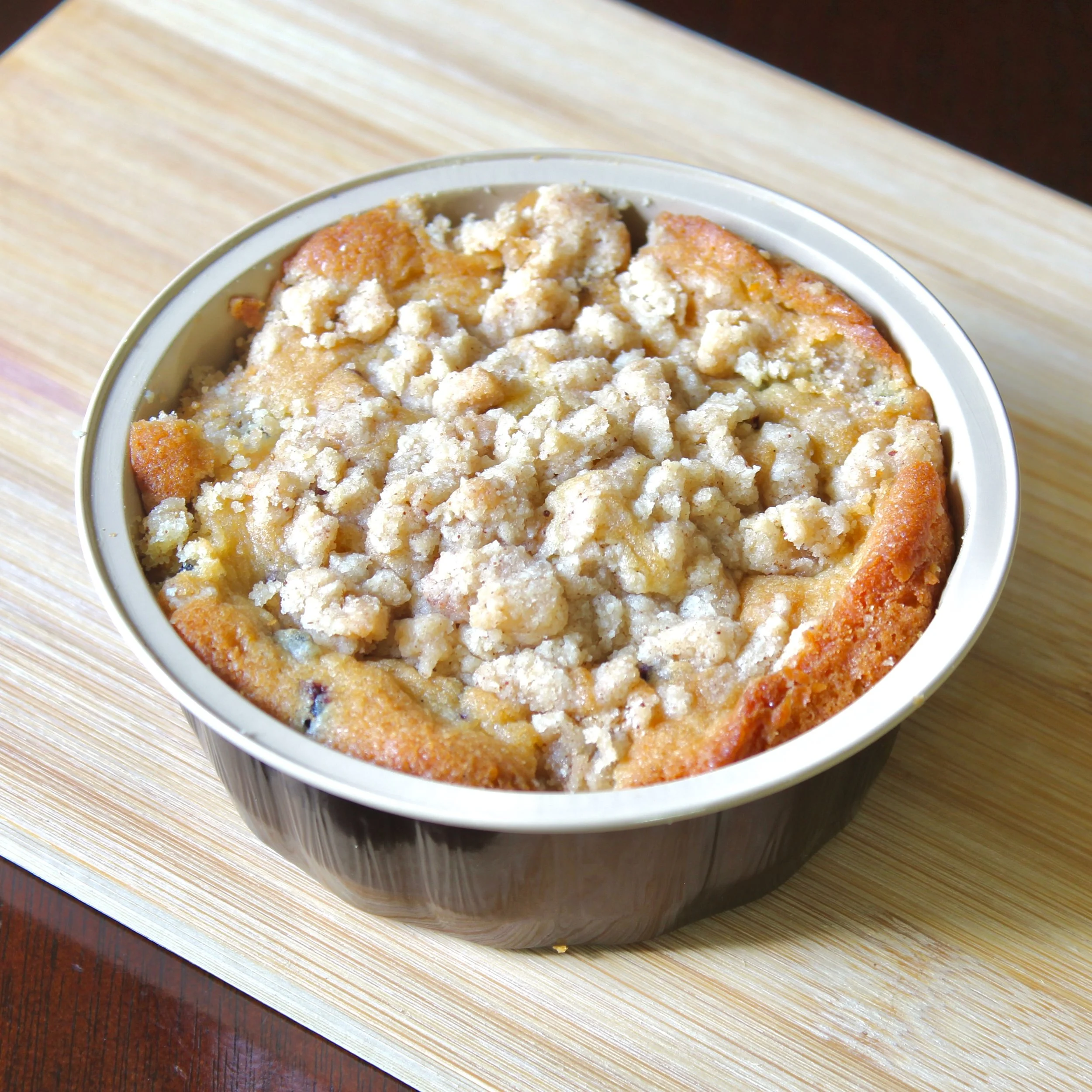 A close-up view of a baked single-serving berry cobbler with rich crumble topping resting on a bamboo cutting board.