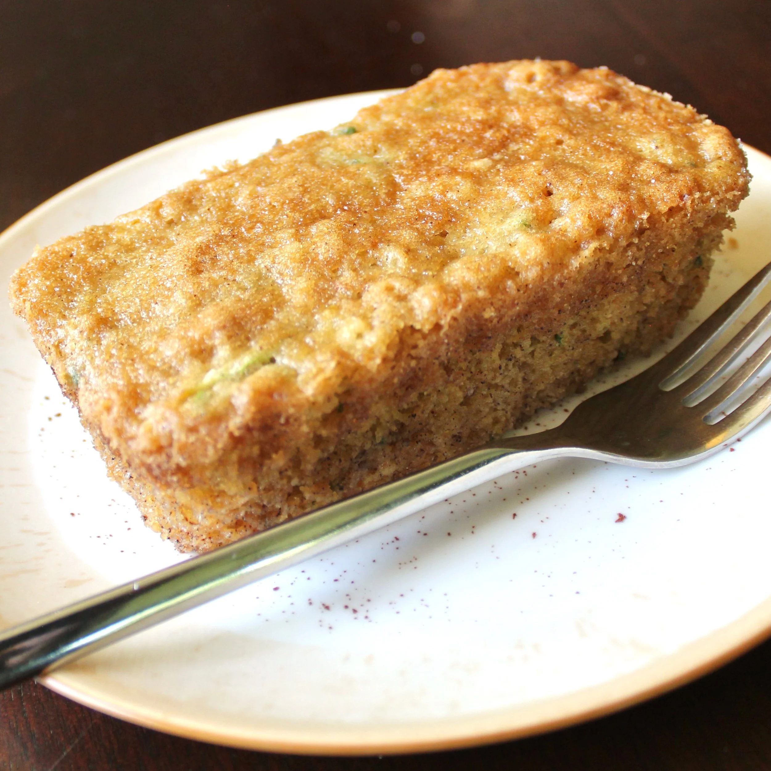 A golden-brown mini loaf of zucchini bread resting on a plate next to a silver fork.