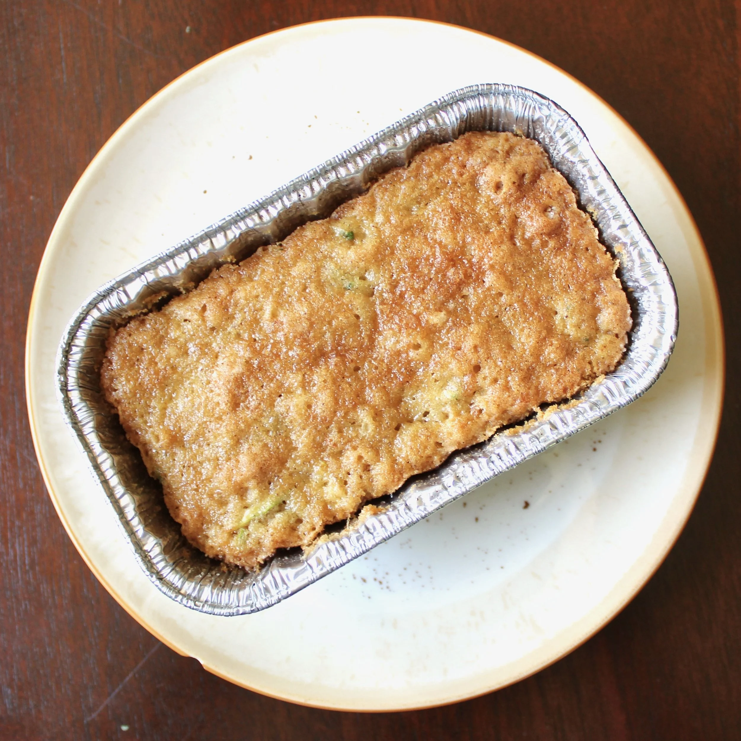 Overhead view of a freshly baked loaf of zucchini bread in a disposable foil baking pan on a plate.
