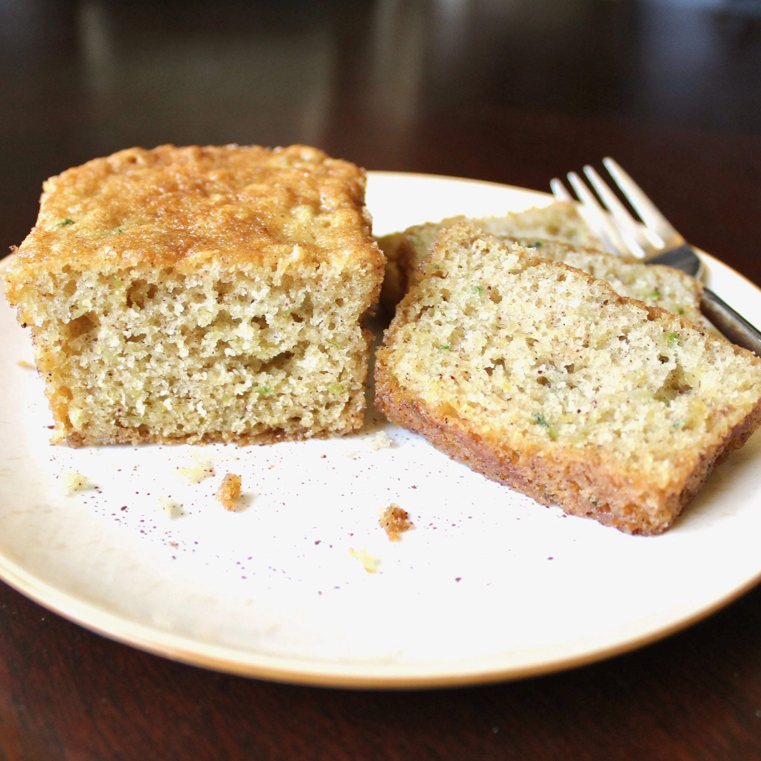 Slices of moist zucchini bread on a white plate with a fork, showing the soft interior crumb texture.