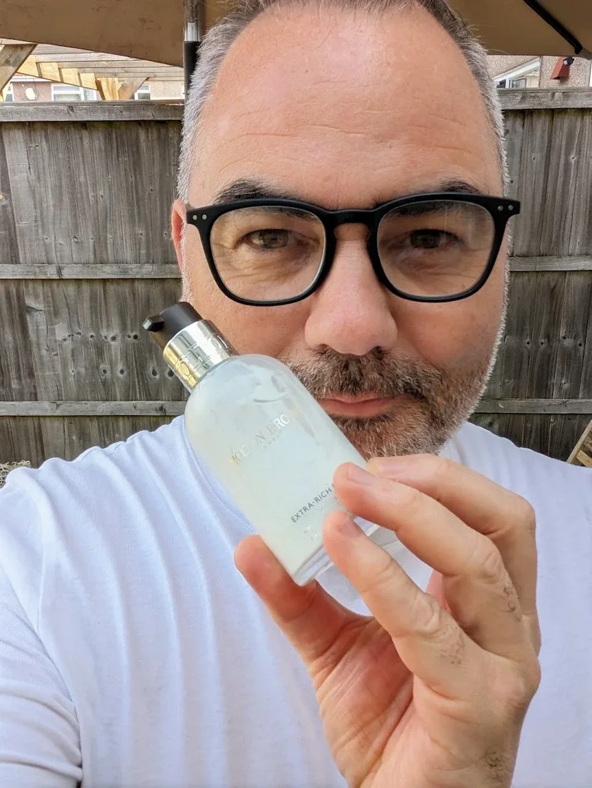 Jerome holding a bottle of Molton Brown Extra-Rich Face Moisturiser while testing it outdoors for a men's skincare review.