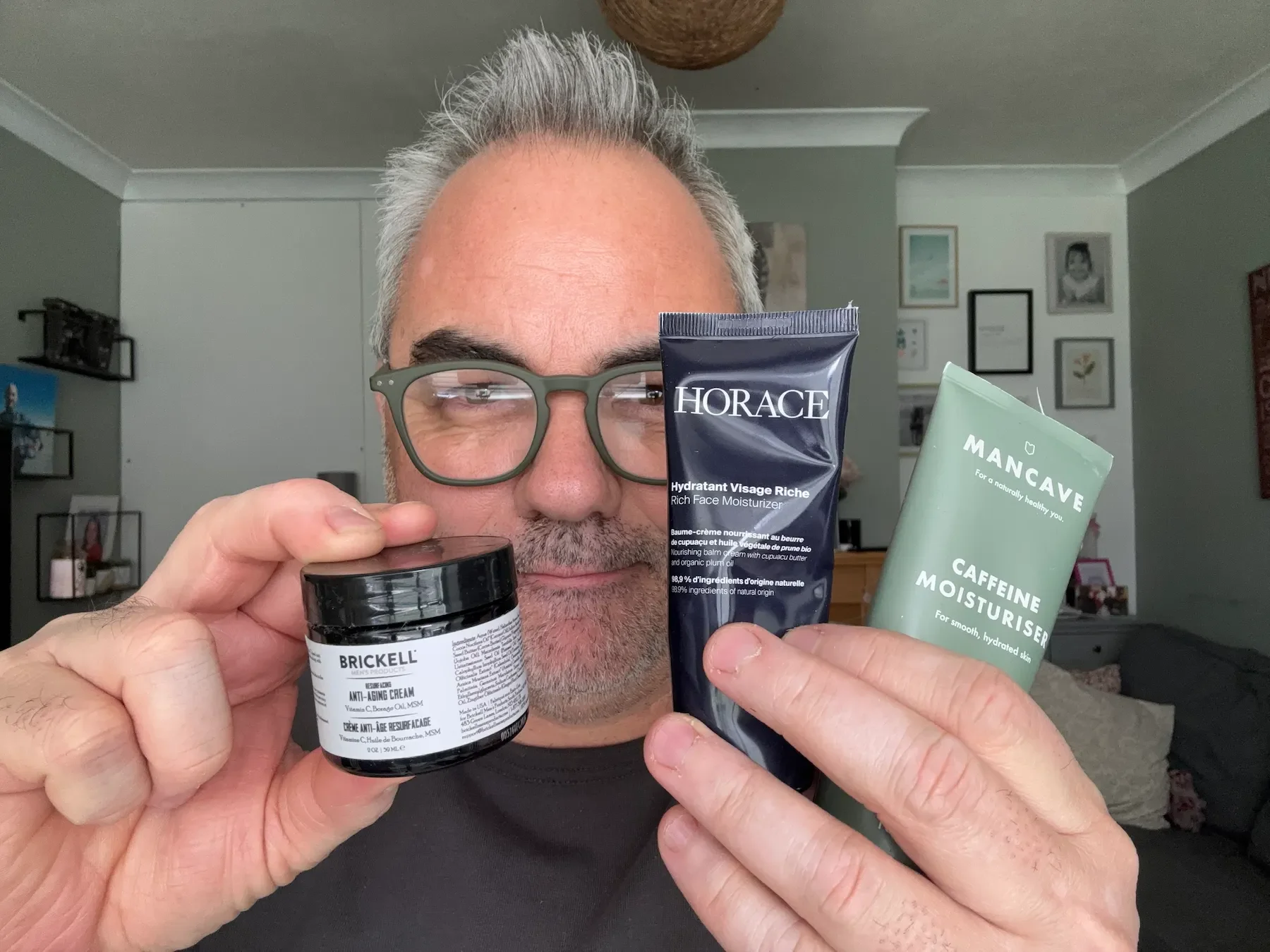 Jerome holding three top-rated face moisturisers for men over 50: Brickell Anti-Aging Cream, Horace Rich Face Moisturiser, and ManCave Caffeine Moisturiser.