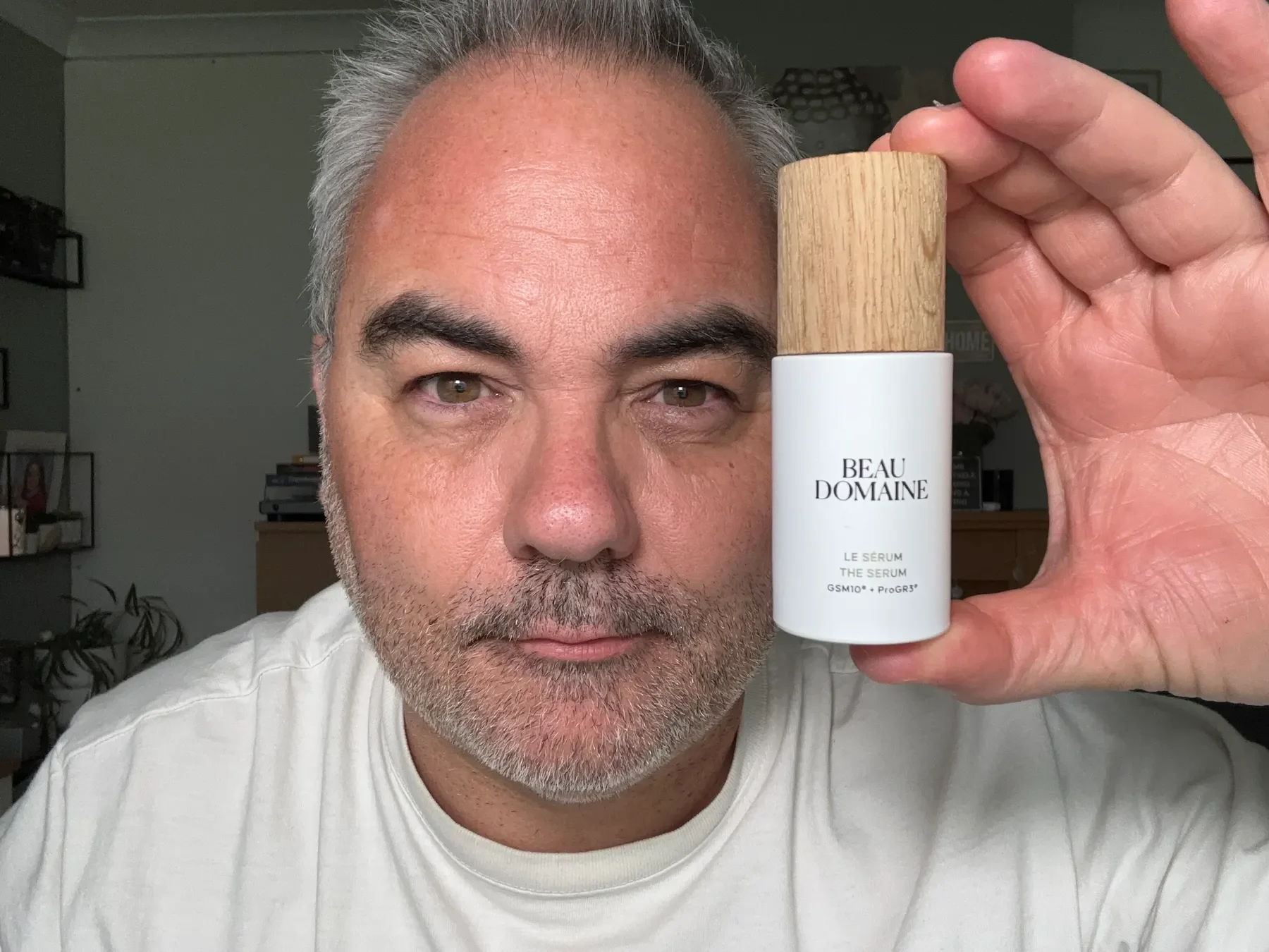 Jerome, a pharmacy-trained expert, holding a bottle of Beau Domaine The Serum, identifying it as the best anti-aging product in the range for men over 50.