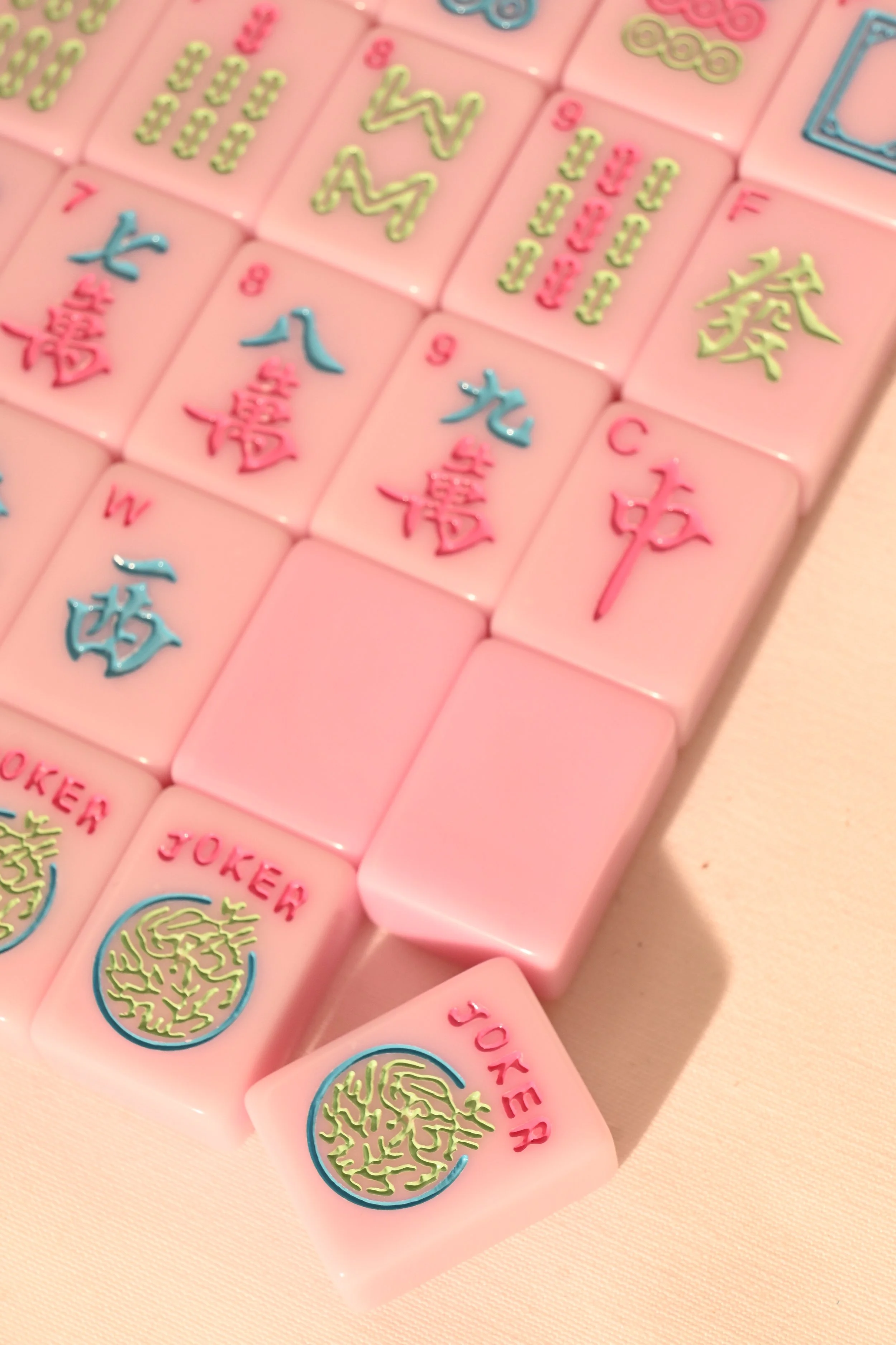 A collection of mahjong tiles with various symbols and characters, primarily pink in color with some blue and green details.