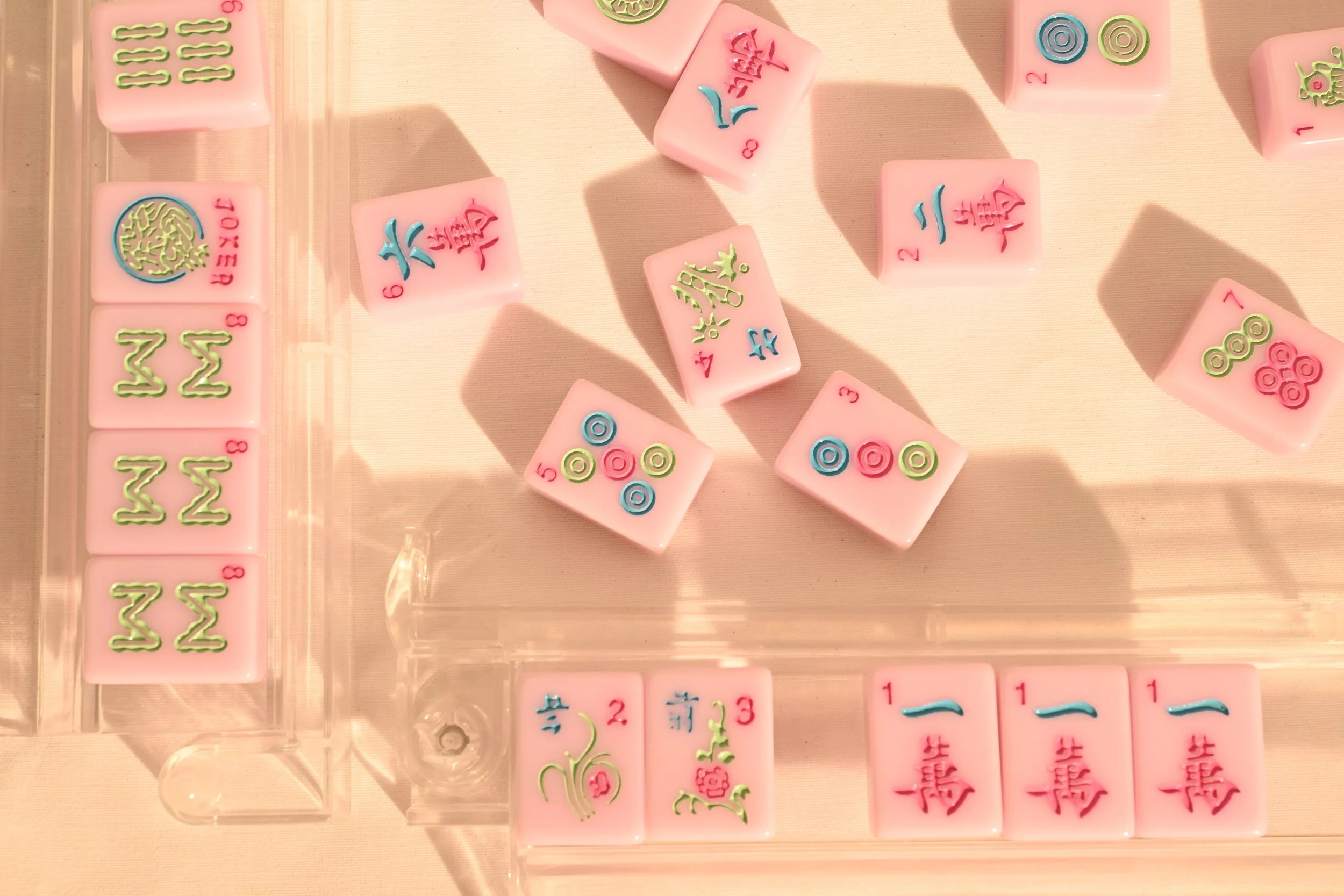 Mahjong tiles arranged on a clear plastic tray, featuring pink tiles with Chinese characters and colorful suit tiles with circles and bamboo symbols.