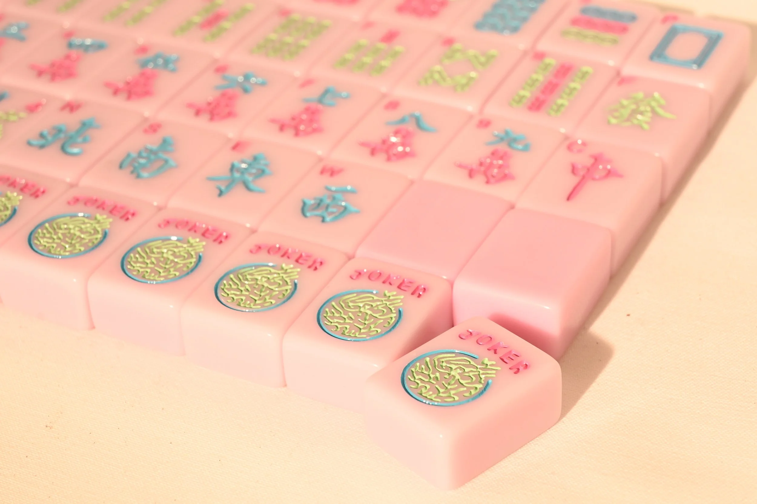 Close-up of pink Mahjong tiles with various colorful symbols and characters on a light-colored surface.