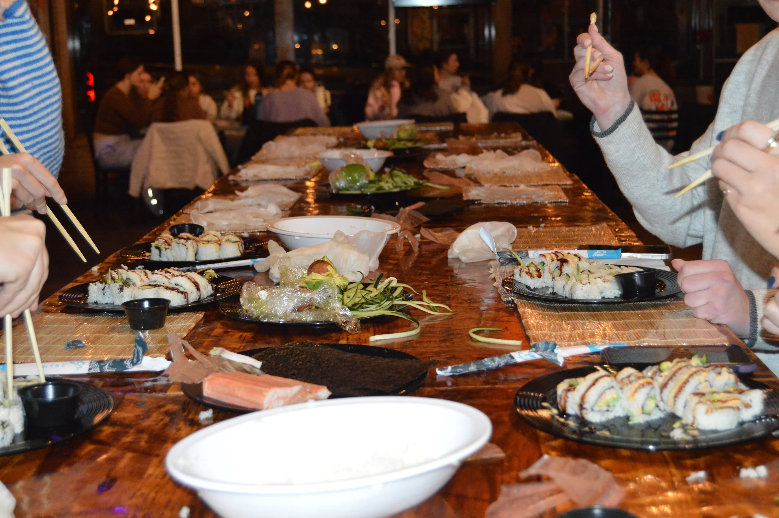 People eating sushi at a long table in a restaurant, with several plates of sushi and chopsticks on the table.