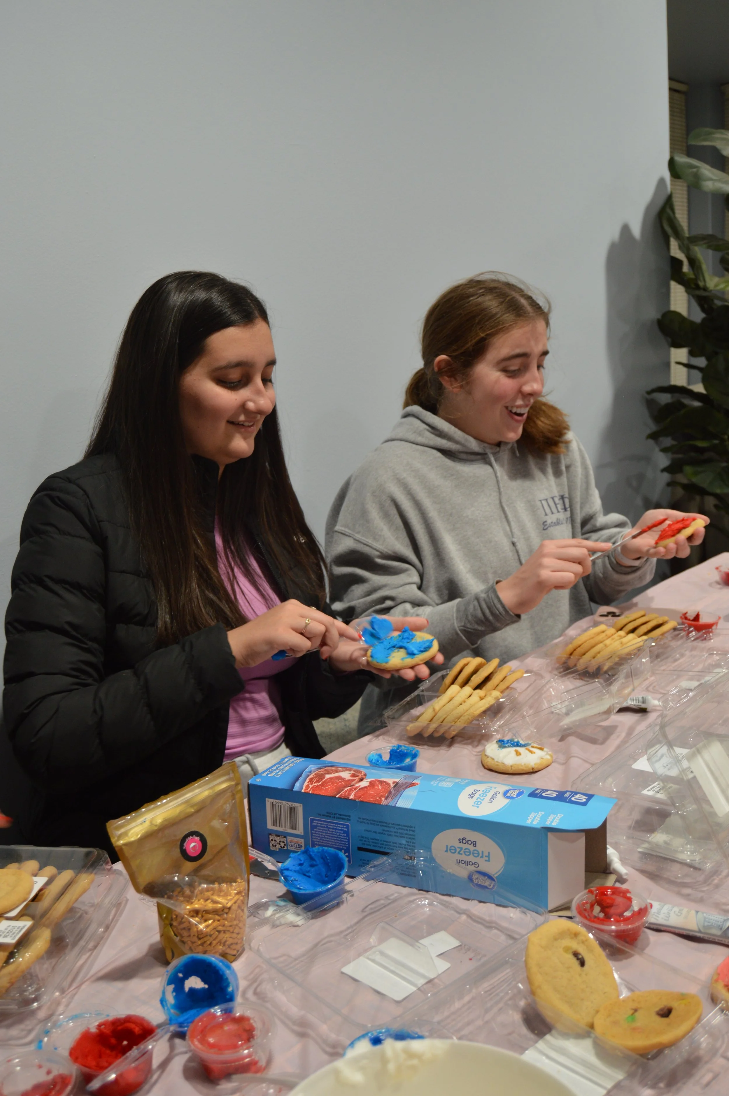 Two women decorating cookies at a table with various baking supplies and cookies.