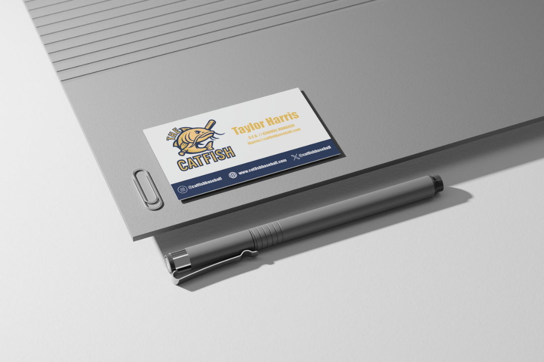 Business card for Taylor Harris, the CEO and general manager of the Catfish basketball team, placed on a gray textured surface with a pen nearby.