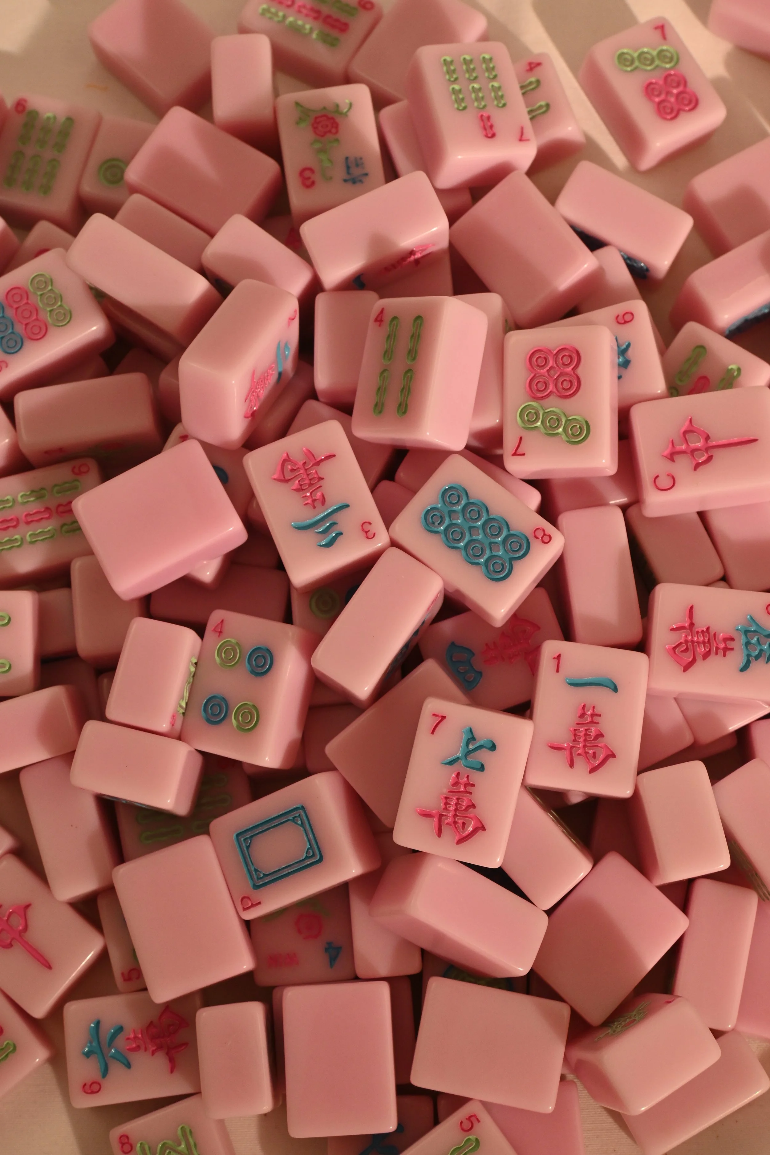 Close-up view of a pile of pink Mahjong tiles with various colorful Chinese characters and symbols.