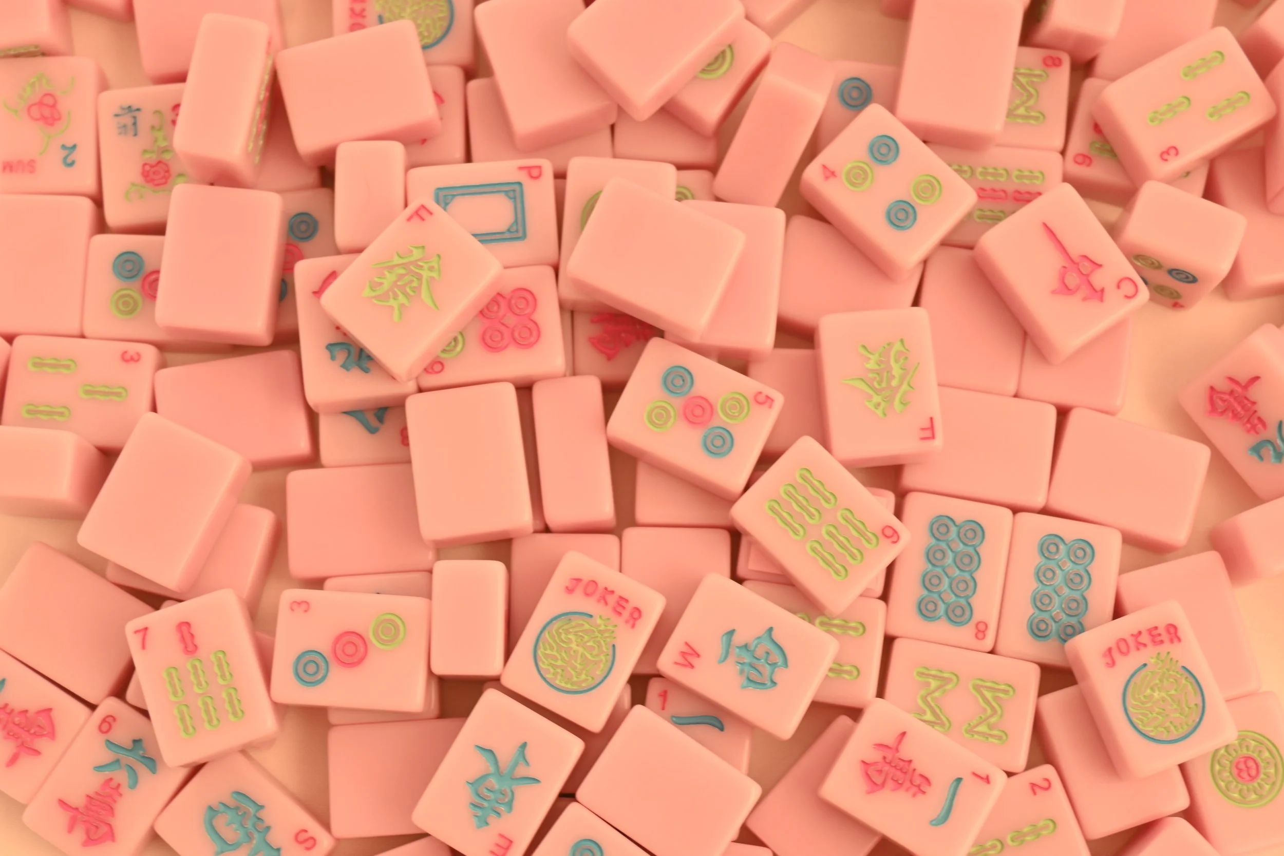 Pink Mahjong tiles with colorful patterns and symbols scattered on a surface.