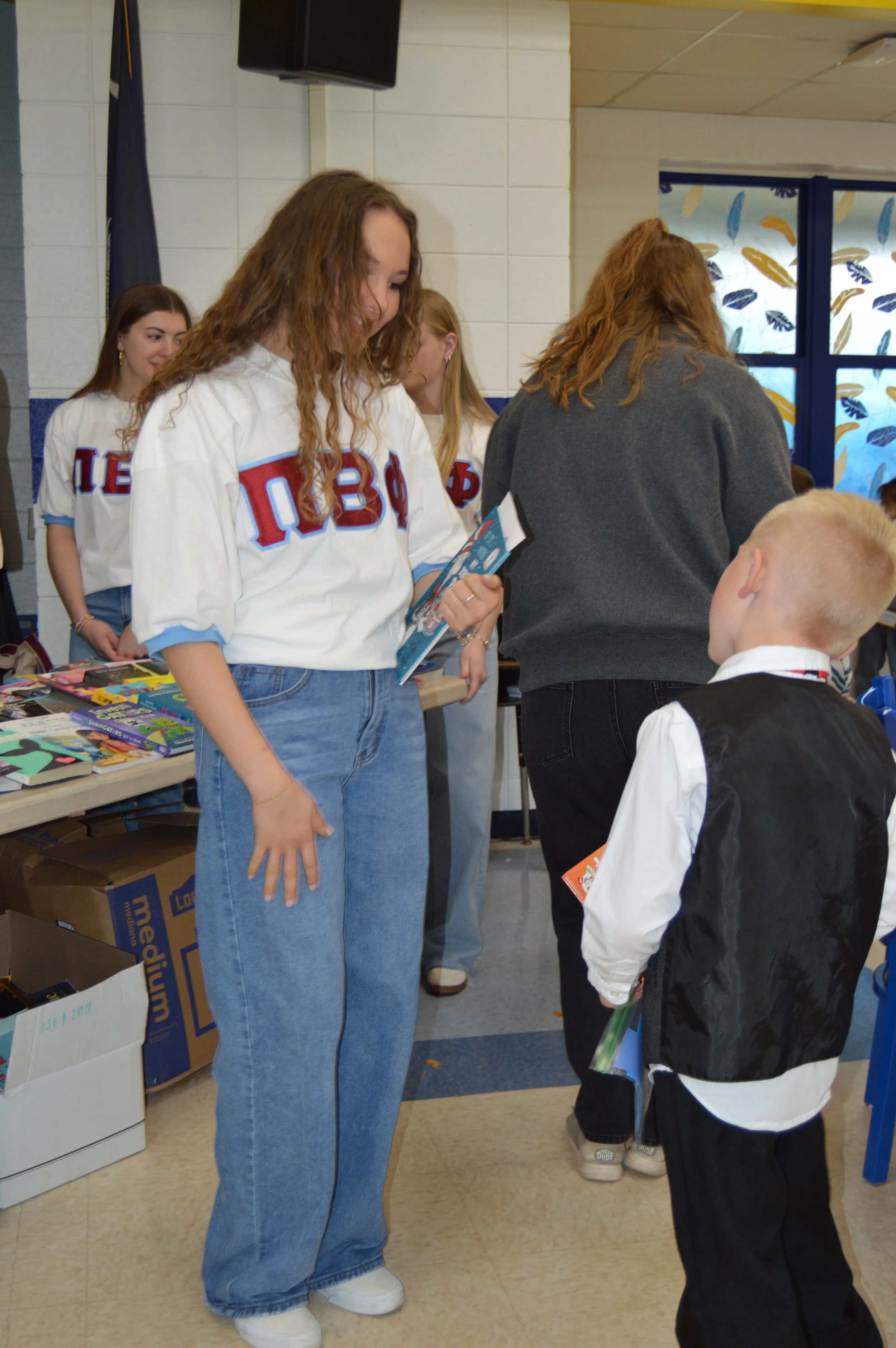 Young woman and young boy interacting at a book donation event, with other women in background and tables filled with books.