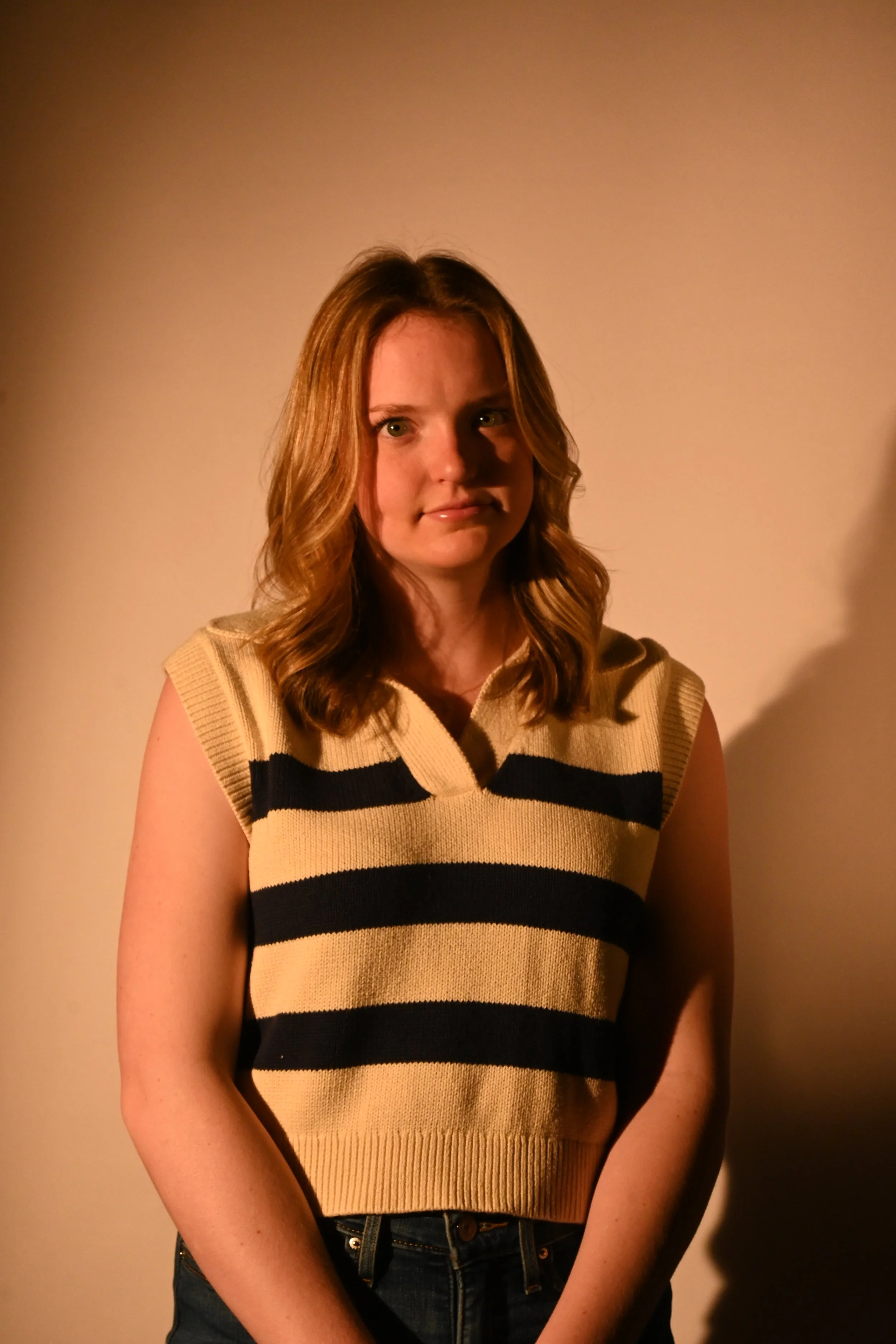 A young woman with wavy red hair wearing a sleeveless yellow and black striped sweater.