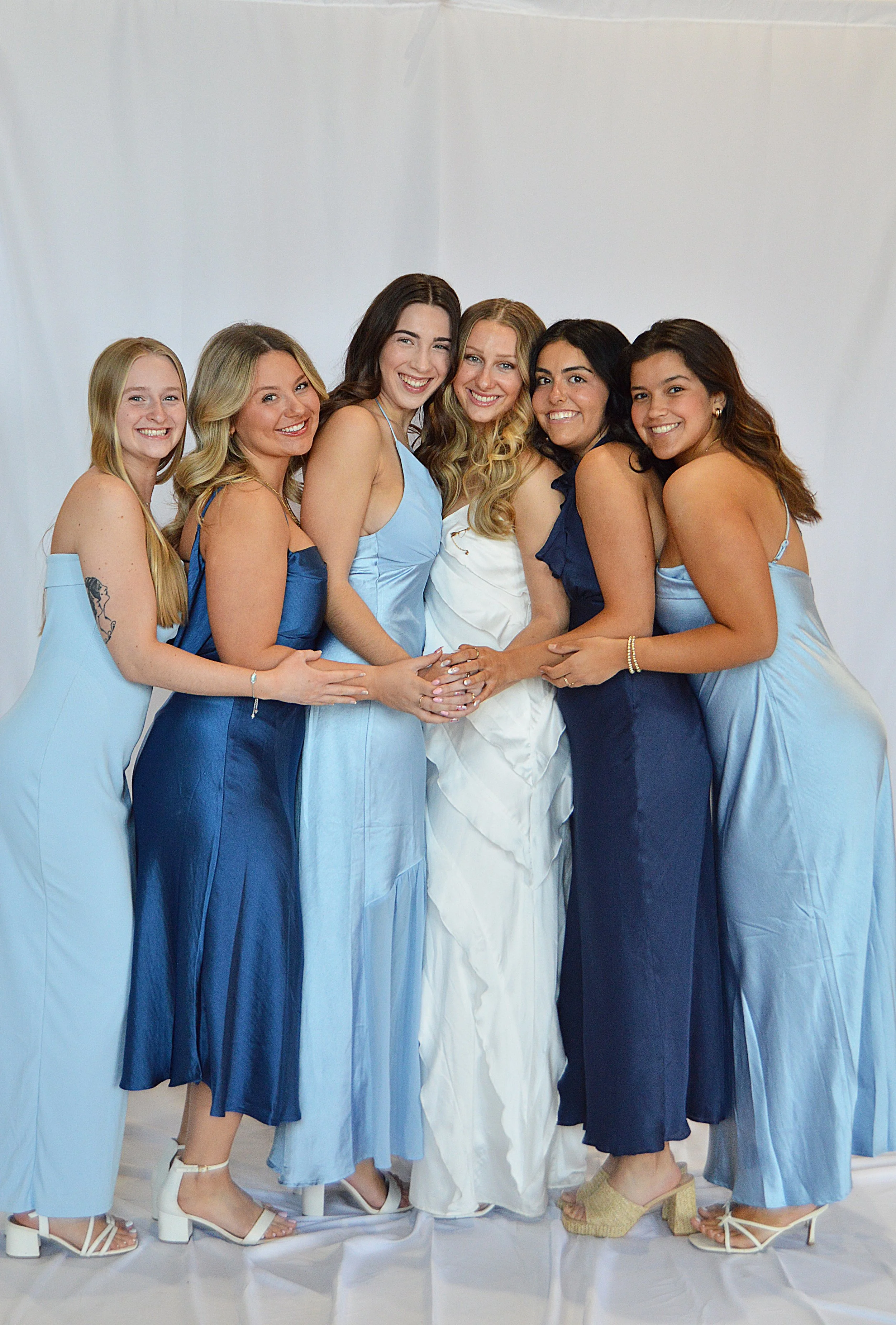 Group of six women wearing blue and white dresses, smiling and posing together in front of a white backdrop.