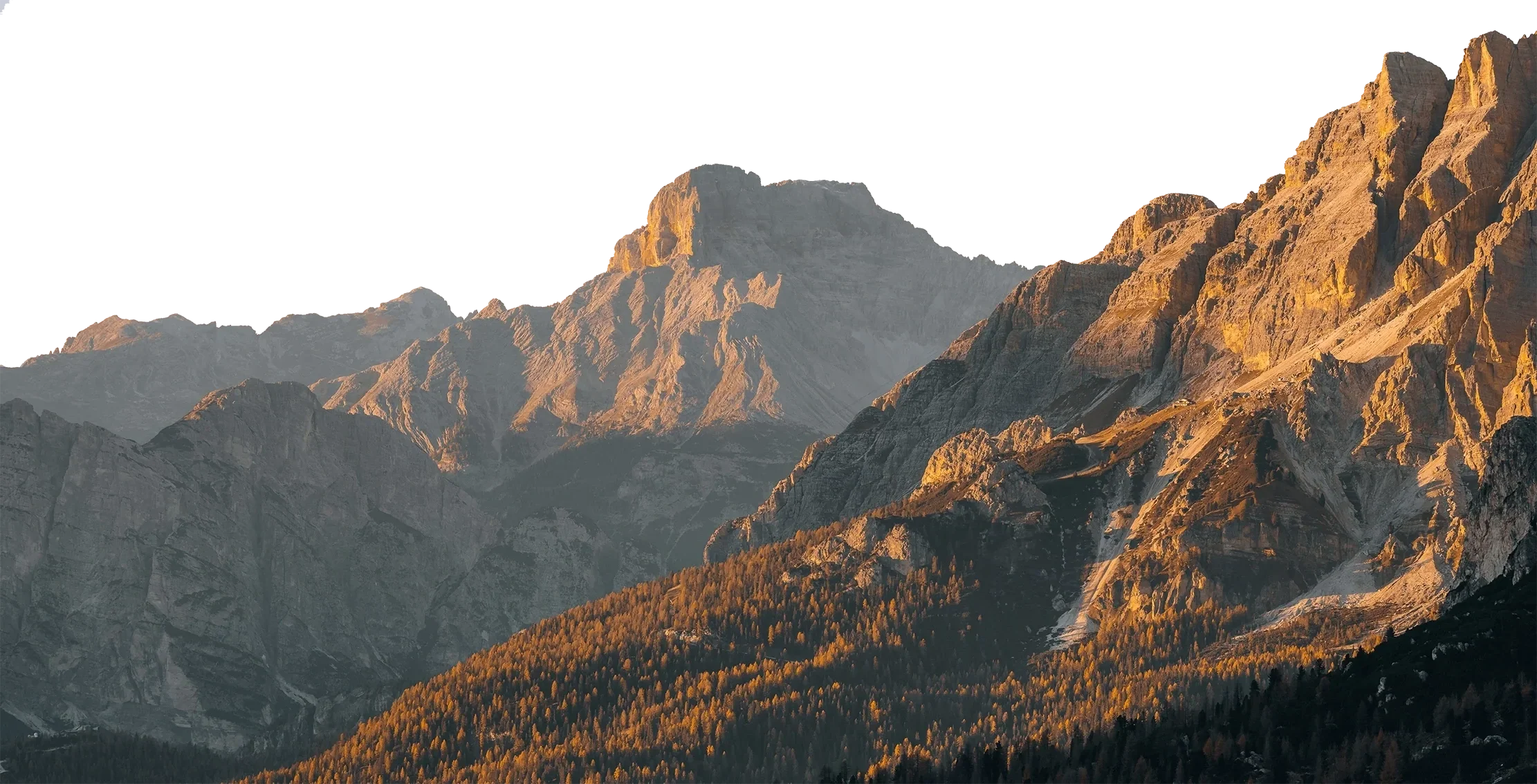 Mountain range with rocky peaks illuminated by sunlight, with forested slopes in the foreground.
