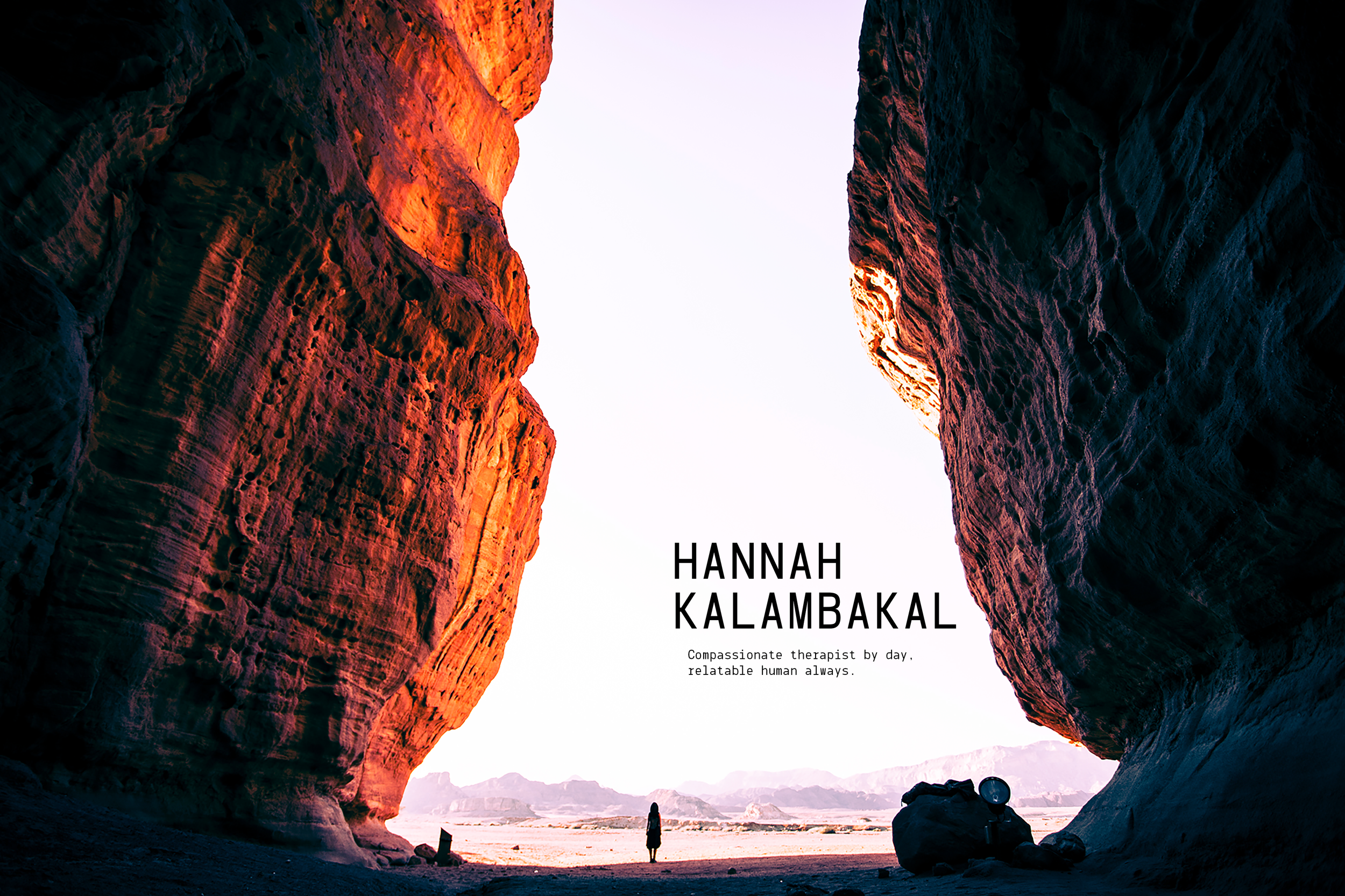 A person standing in a desert canyon at sunset, with tall, rugged rock formations on either side and mountains in the distance.