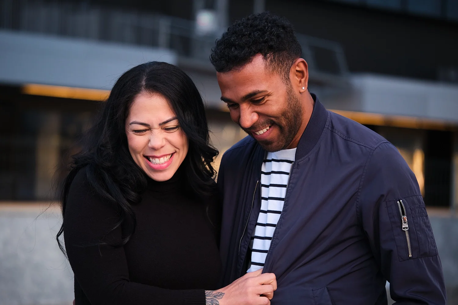A woman and a man smiling and laughing together outdoors, close-up portrait.