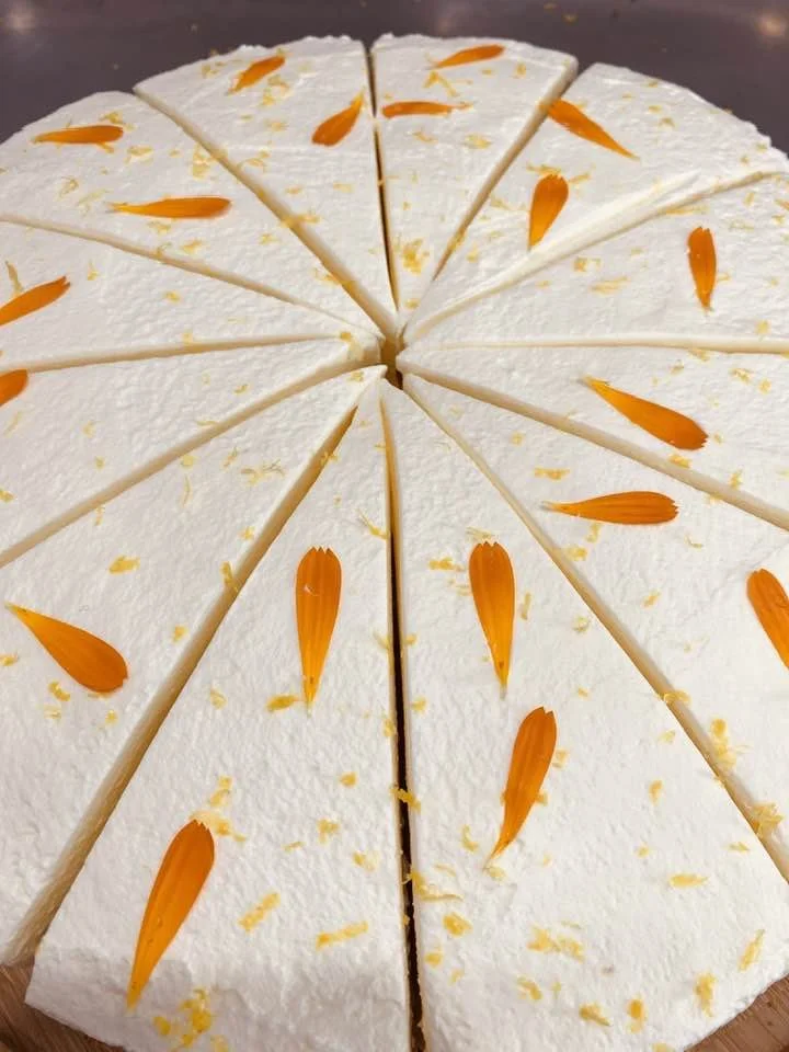 A sliced white cake decorated with orange flower petals and yellow zest.