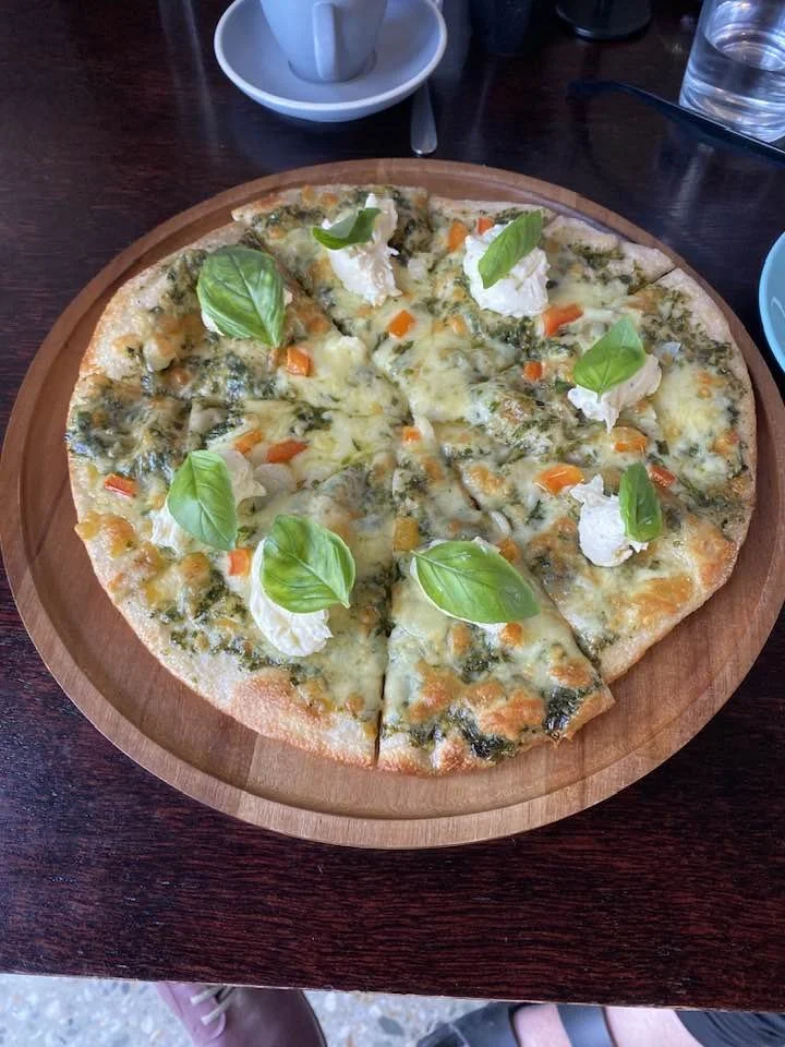 A cheese and vegetable pizza topped with basil leaves, served on a wooden platter.