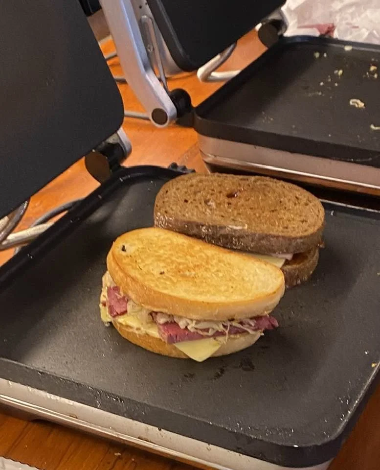 A Reuben sandwich ,placed on a black griddle.