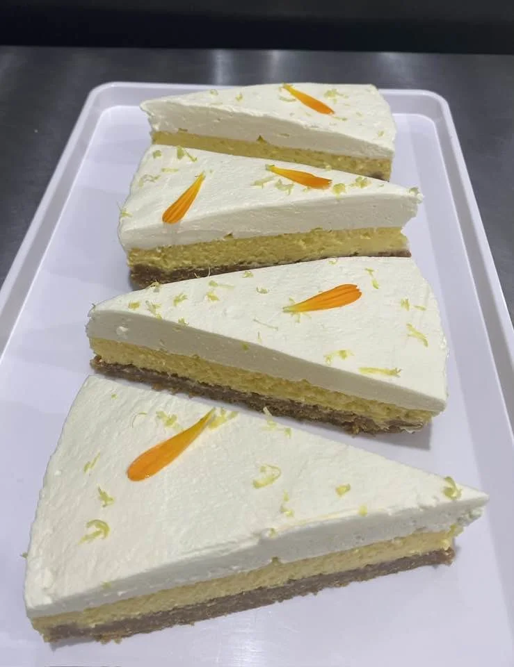 Four slices of lemon cheesecake with white frosting and orange petal decorations on a white tray.