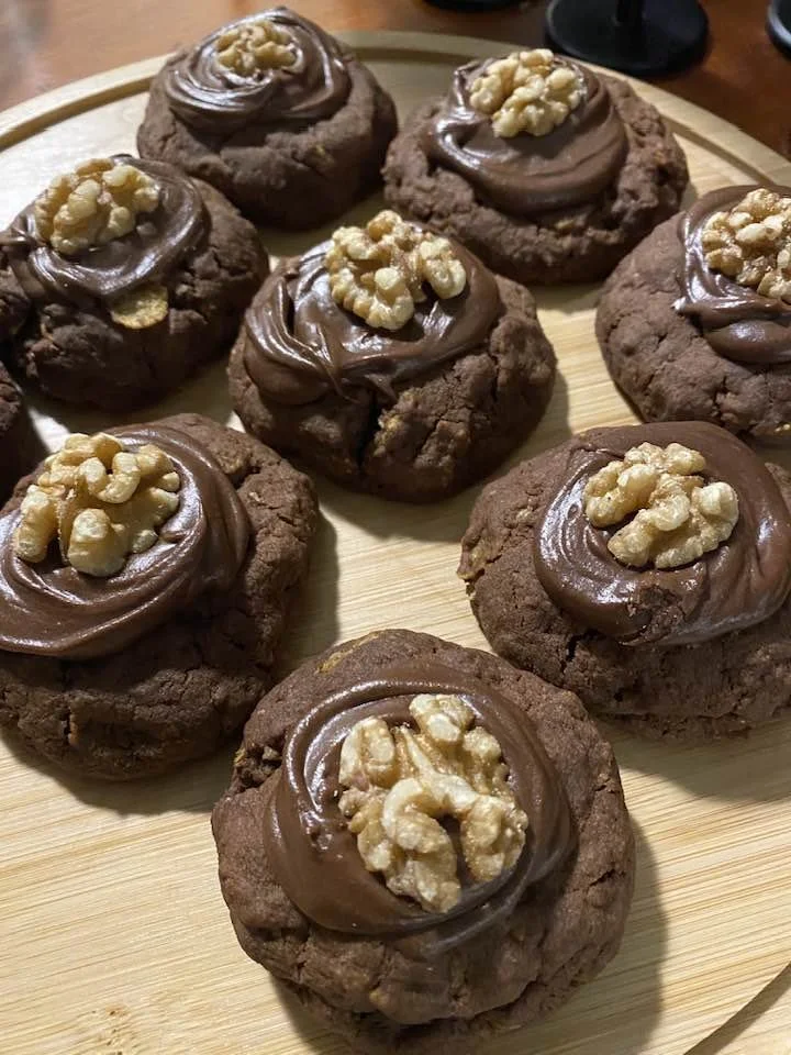 A plate of chocolate afghan cookies topped with swirls of chocolate frosting and sprinkled with chopped walnuts.