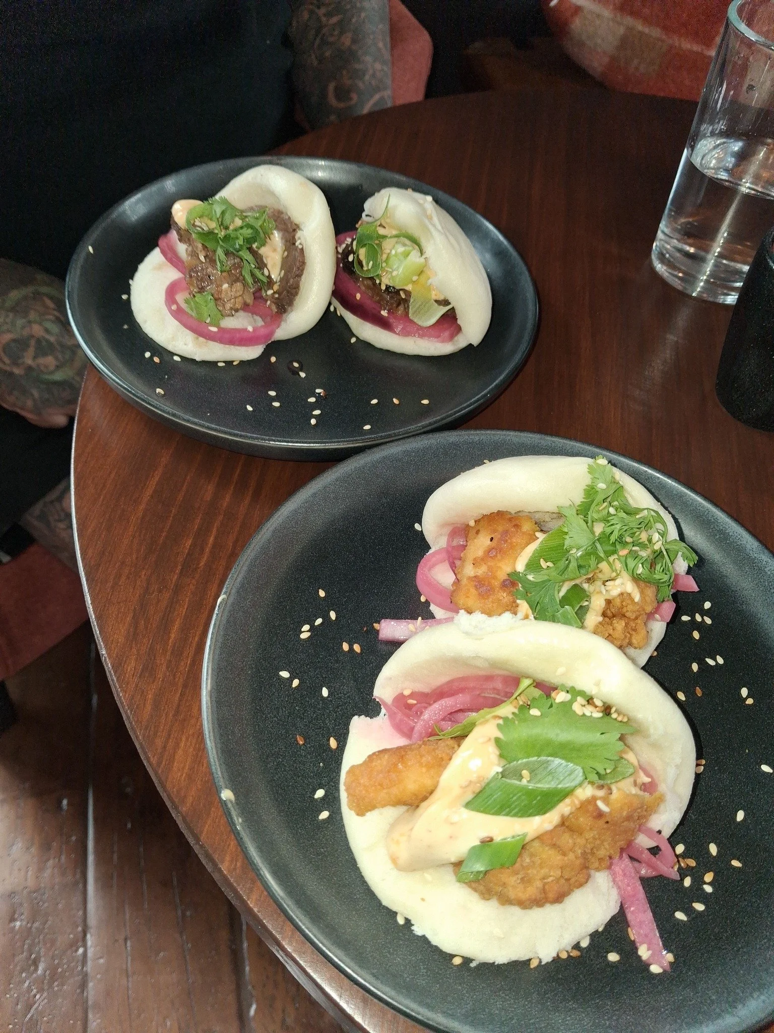 Close-up of two Asian steamed buns with various fillings and garnishes, served on black plates.