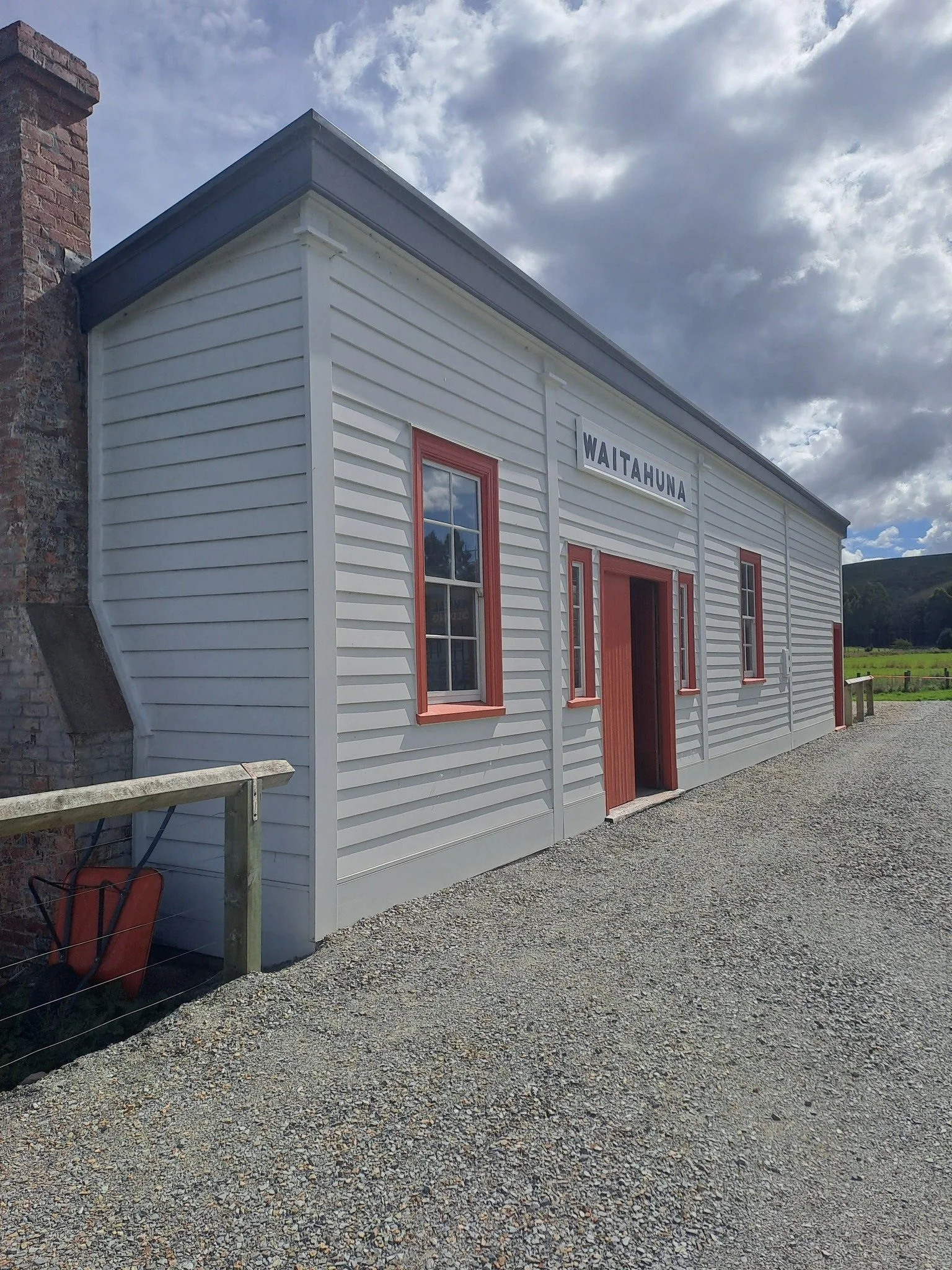 Waitahuna Station Museum.  A white building with pink window frames and a sign that reads 'WAITAHUNA' under a partly cloudy sky.