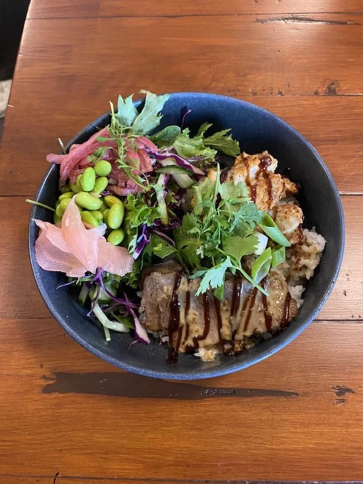 Bowl of mixed salad and grilled chicken with sauce, served on a wooden table.