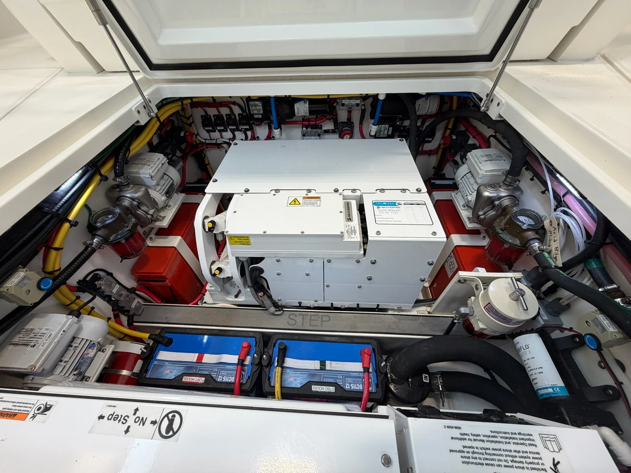 The image shows an open battery compartment, likely on a boat or a yacht, filled with various electrical components, wiring, and batteries.
