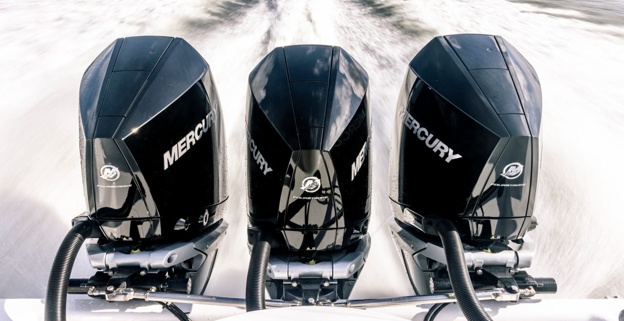 Three Mercury outboard motors mounted on a boat propelling through water.