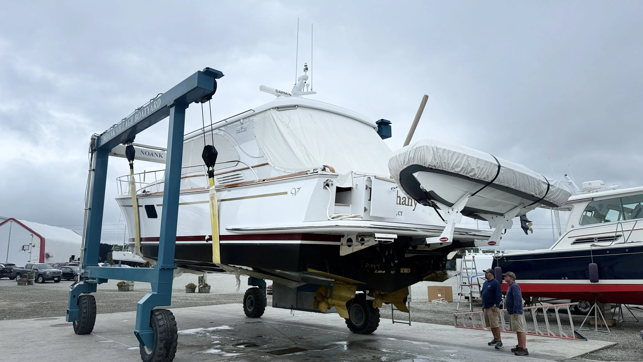 A large white yacht on a boat lift at a marina, with two men standing nearby and overcast skies above.