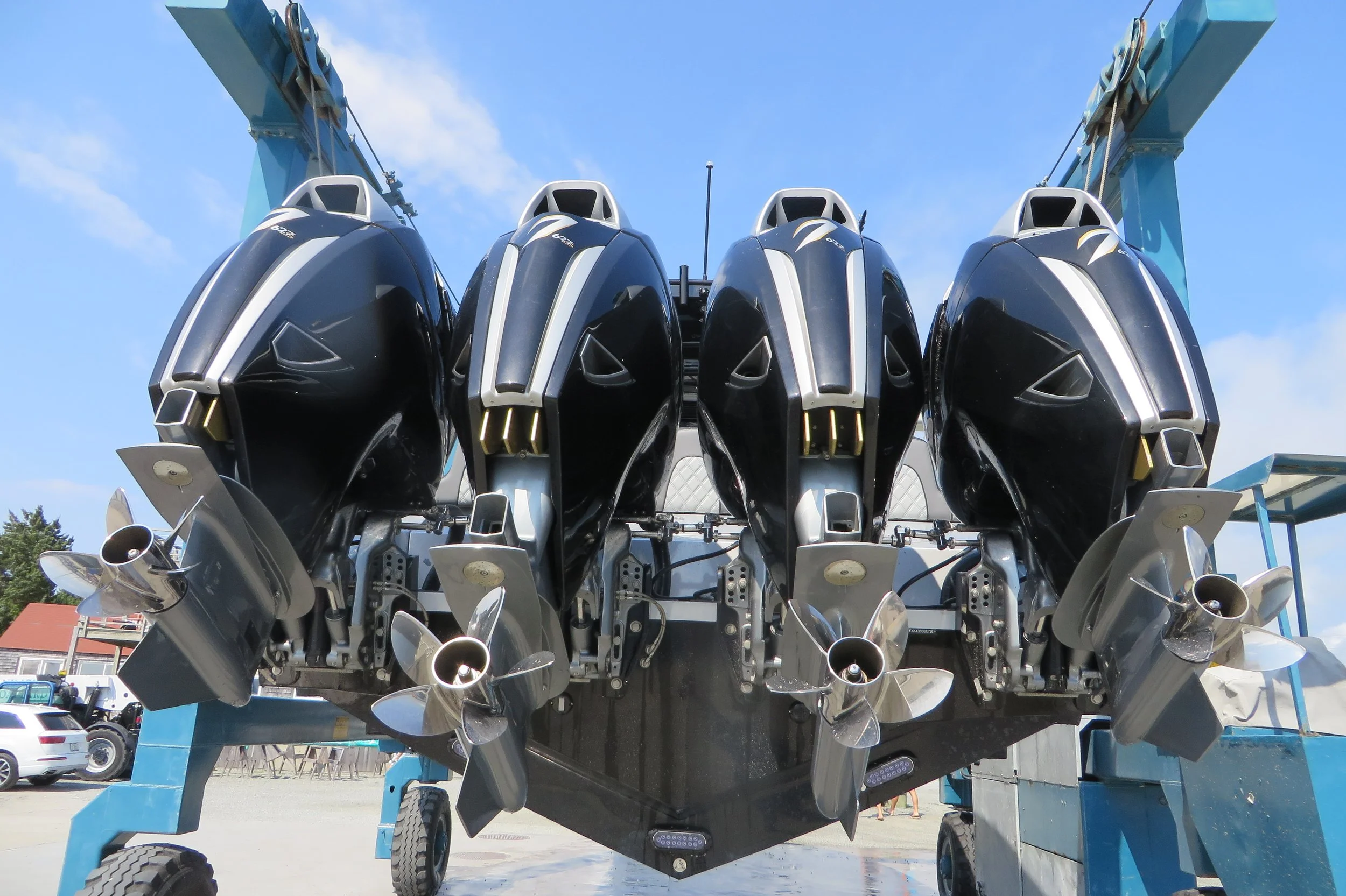 Close-up view of a large boat or yacht propeller system with multiple metallic propellers arranged in front of a blue crane structure, set against a clear blue sky.
