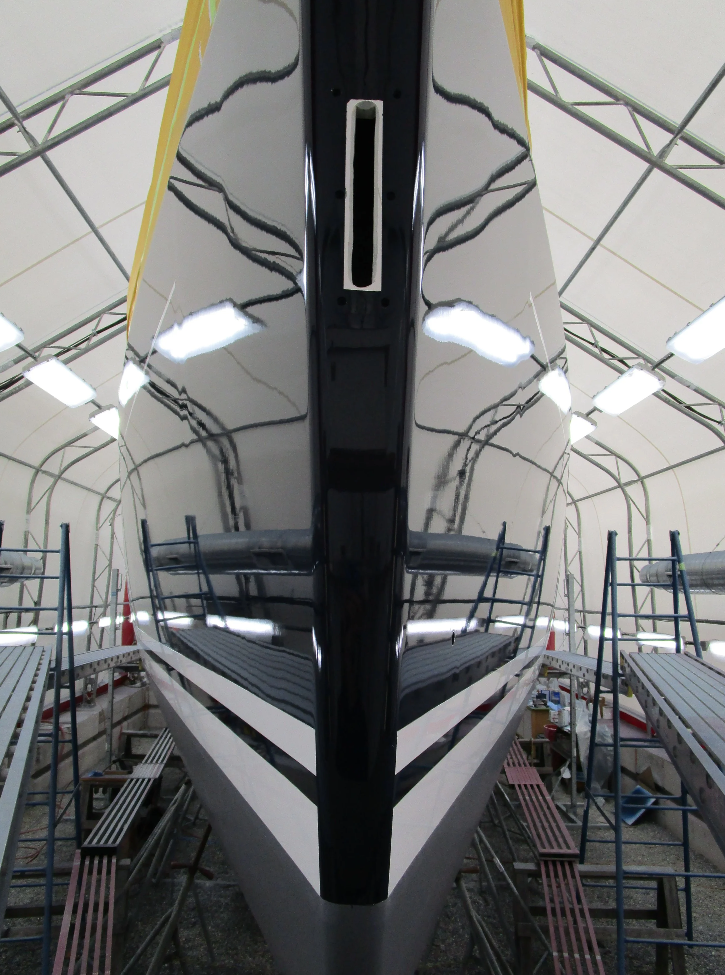 A large boat or ship under construction in an indoor boat yard, with scaffolding and workbenches surrounding it.